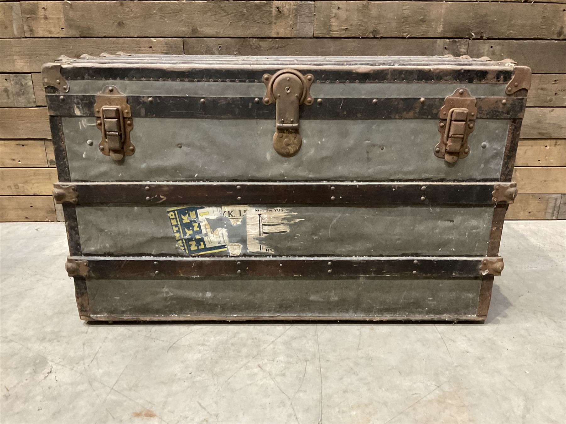 Early 20th century wood and metal bound zinc travelling trunk, hinged top with three clasps, decorated with period luggage labels
