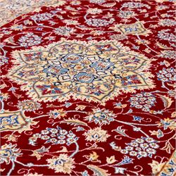 Central Persian Nain hand-knotted rug, crimson field, with central ornate ivory medallion with scrolling arabesques and flowering vine ornaments within a dense floral lattice framed by pale blue corner spandrels and enclosed with an ivory border of scrolling vine and palmette decoration between multiple guard stripes, with cotton fringe ends 
