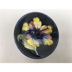 Moocroft small footed circular dish decorated in the Hibiscus pattern upon cobalt blue ground, with Queen Mary paper label beneath, together with a smaller example decorated in the Orchid pattern with impressed and printed W.Moorcroft marks beneath, largest, D9cm, (2)