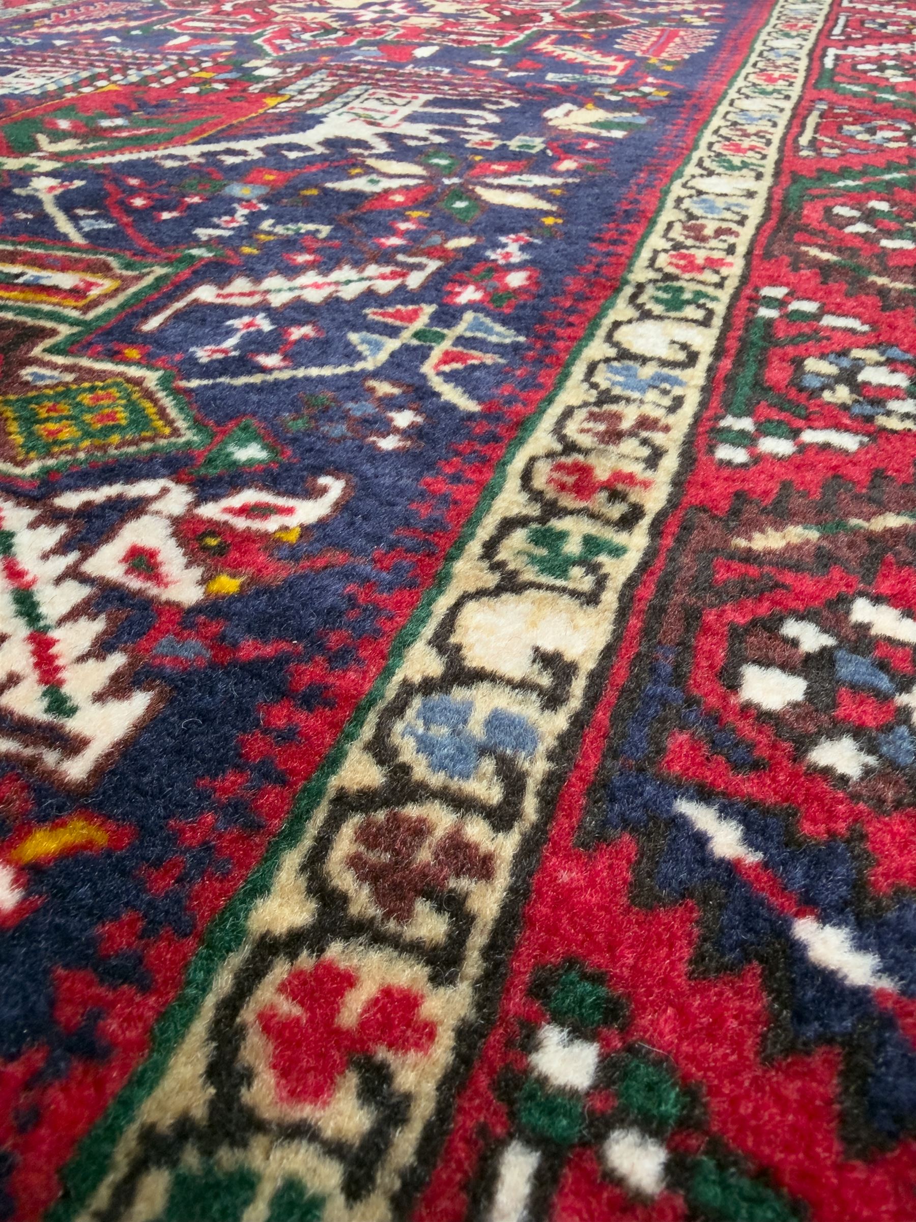 Northwestern Persian Heriz hand-knotted runner, dark indigo field with a series of linked stepped medallions in madder red, ivory, and green, flanked by angular floral motifs, within a madder red border of stylized rosettes and geometric vine motifs 405cm x 95cm