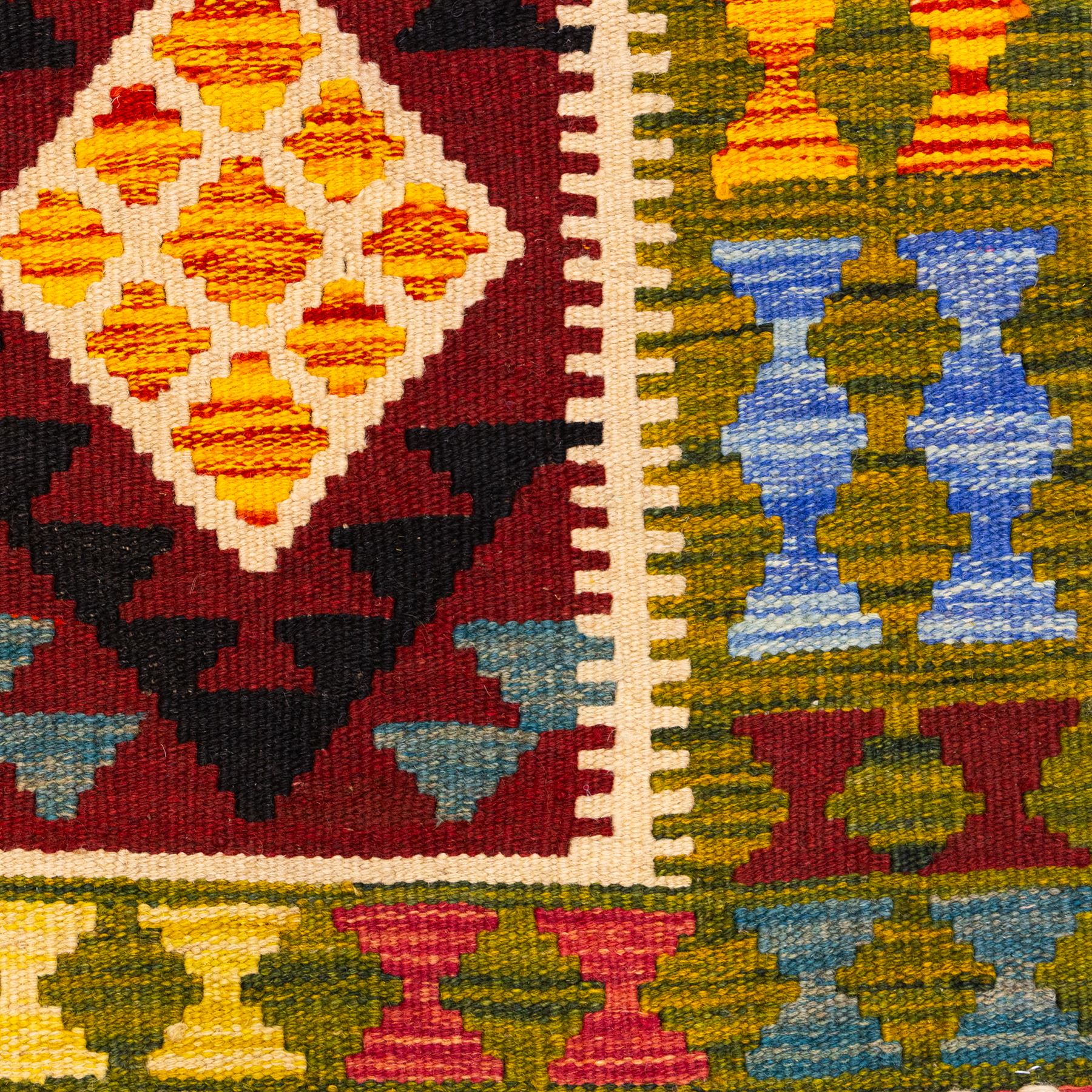 Afghan Maimana flatweave kilim, central crimson field features a large bold nested diamond motif and stylized geometric lozenge patterns on olive purple, blue, yellow and green tone ground, border stripe in teal ground, and fringe