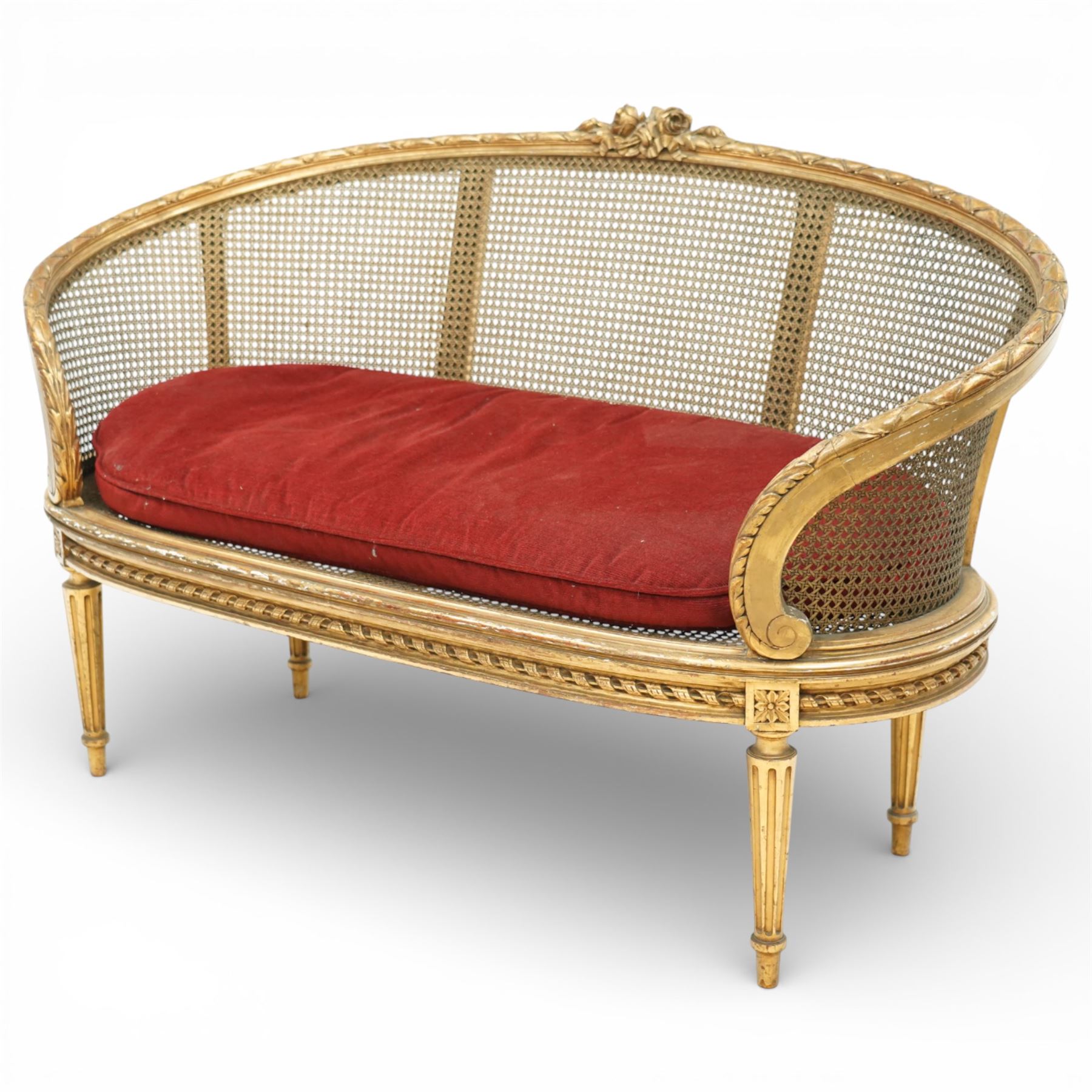 19th century giltwood and gesso settee, with shaped crest rail centred by carved floral detail, the cane back with vertical divisions, upholstered seat with loose cushion, raised on fluted tapering legs