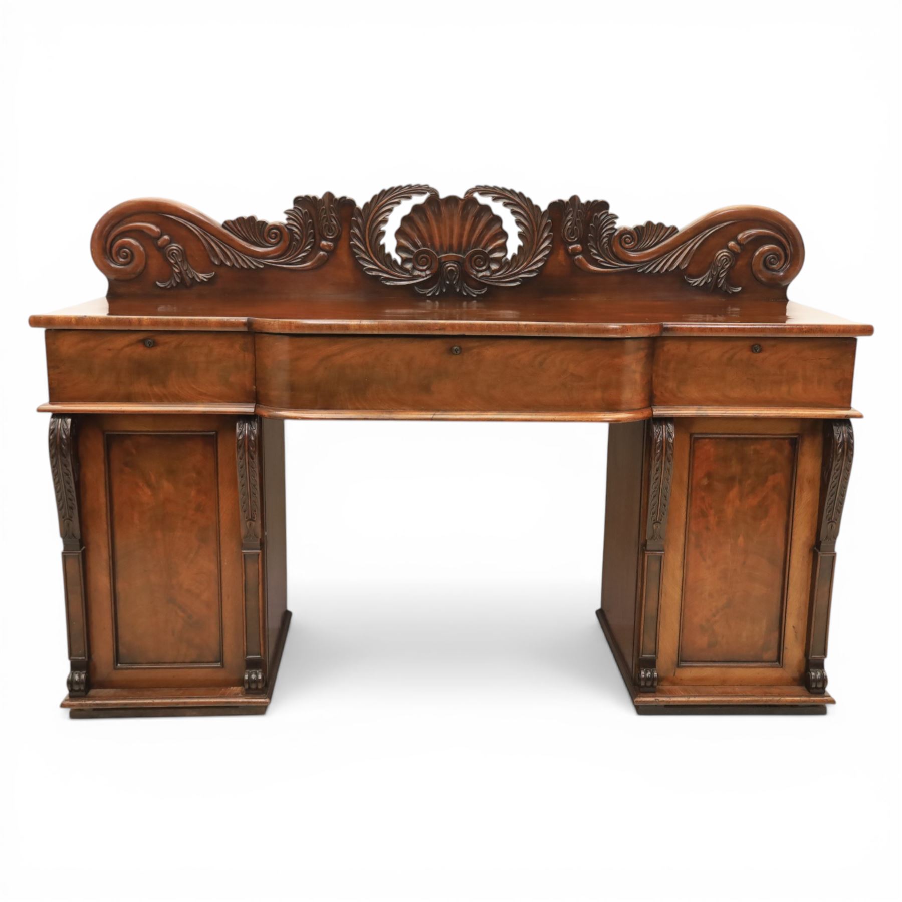 Mid Victorian mahogany pedestal sideboard, the rectangular top with raised back centred by a carved shell within scrolling acanthus and foliate cresting, over a central shaped frieze drawer flanked by two short drawers, above a kneehole recess, flanked by panelled cupboard doors with carved corbel supports, enclosing shelved interiors