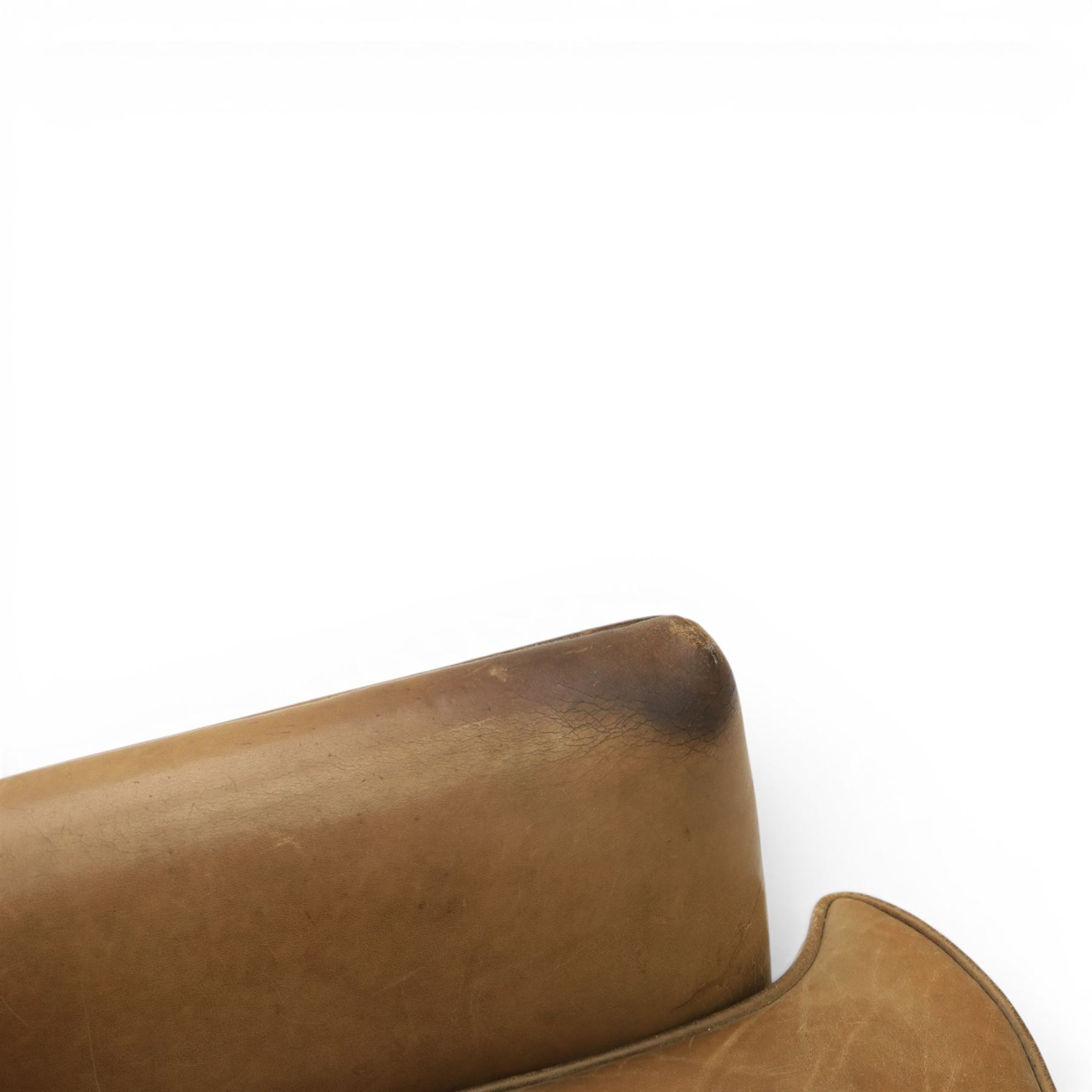 20th century tan leather armchair, the curved wing back above low square arms, shaped loose seat cushion with piped edge, close-nailed side detail, raised on concealed castors
