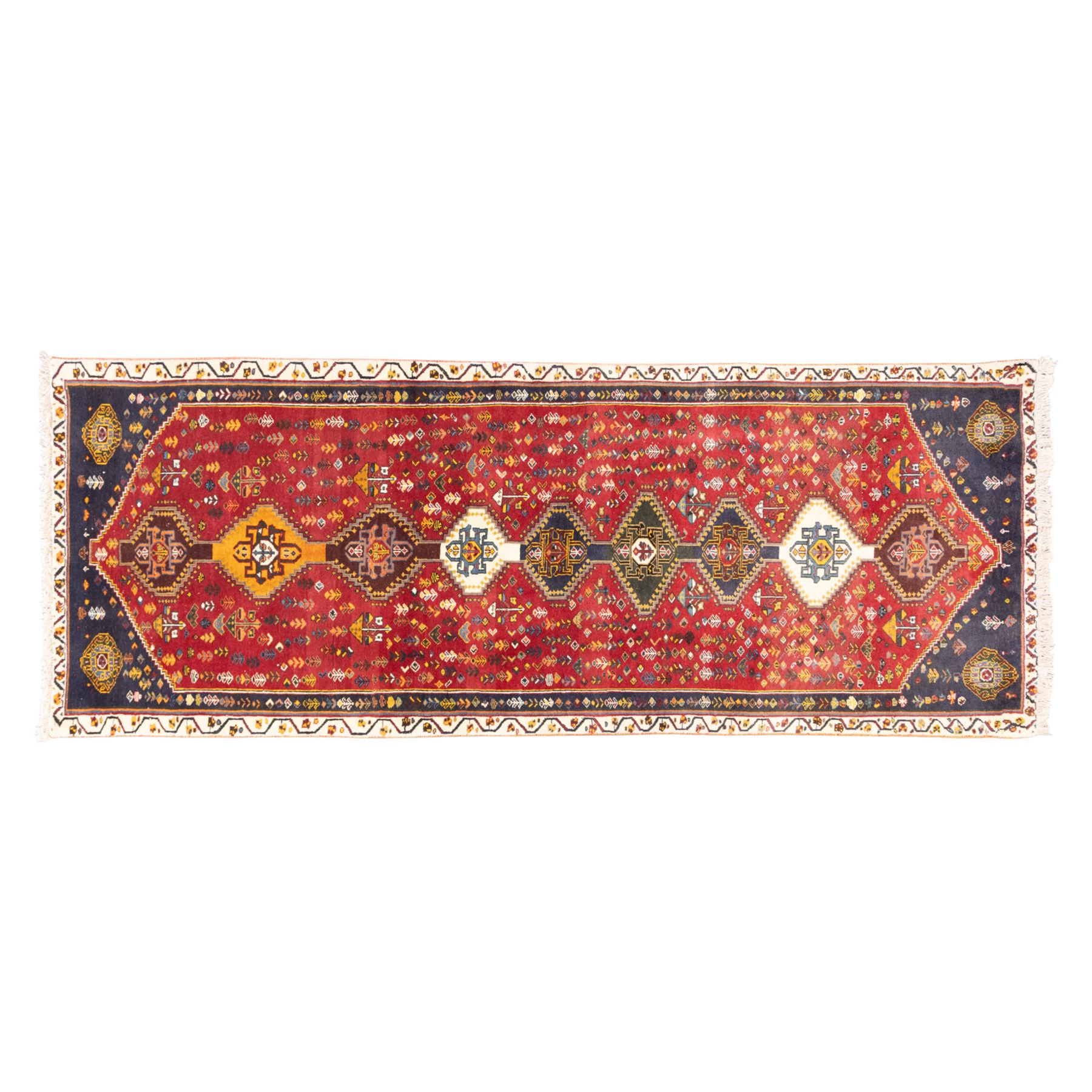 South West Persian hand-knotted Qashgai runner, madder-red field with a central column of linked diamond medallions in tones of indigo, ochre, ivory, and green, surrounded by stylized floral and boteh motifs within a cream border of angular vines and serrated devices, with cotton fringe ends   