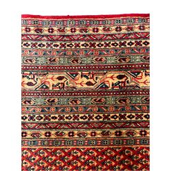 Persian Arak crimson ground carpet, the field decorated profusely with small repeating Boteh motifs, enclosed by multiple border bands decorated with repeating geometric and hook motifs