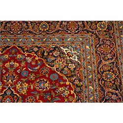 Central Persian Kashan hand-knotted carpet, crimson field with central cusped medallion in ivory, pale blue and indigo, issuing a network of scrolling arabesques, palmettes, and floral sprays, with conforming spandrels, main border of scrolling vinery and stylized palmettes, framed by multiple guard borders, with cotton fringe ends 
