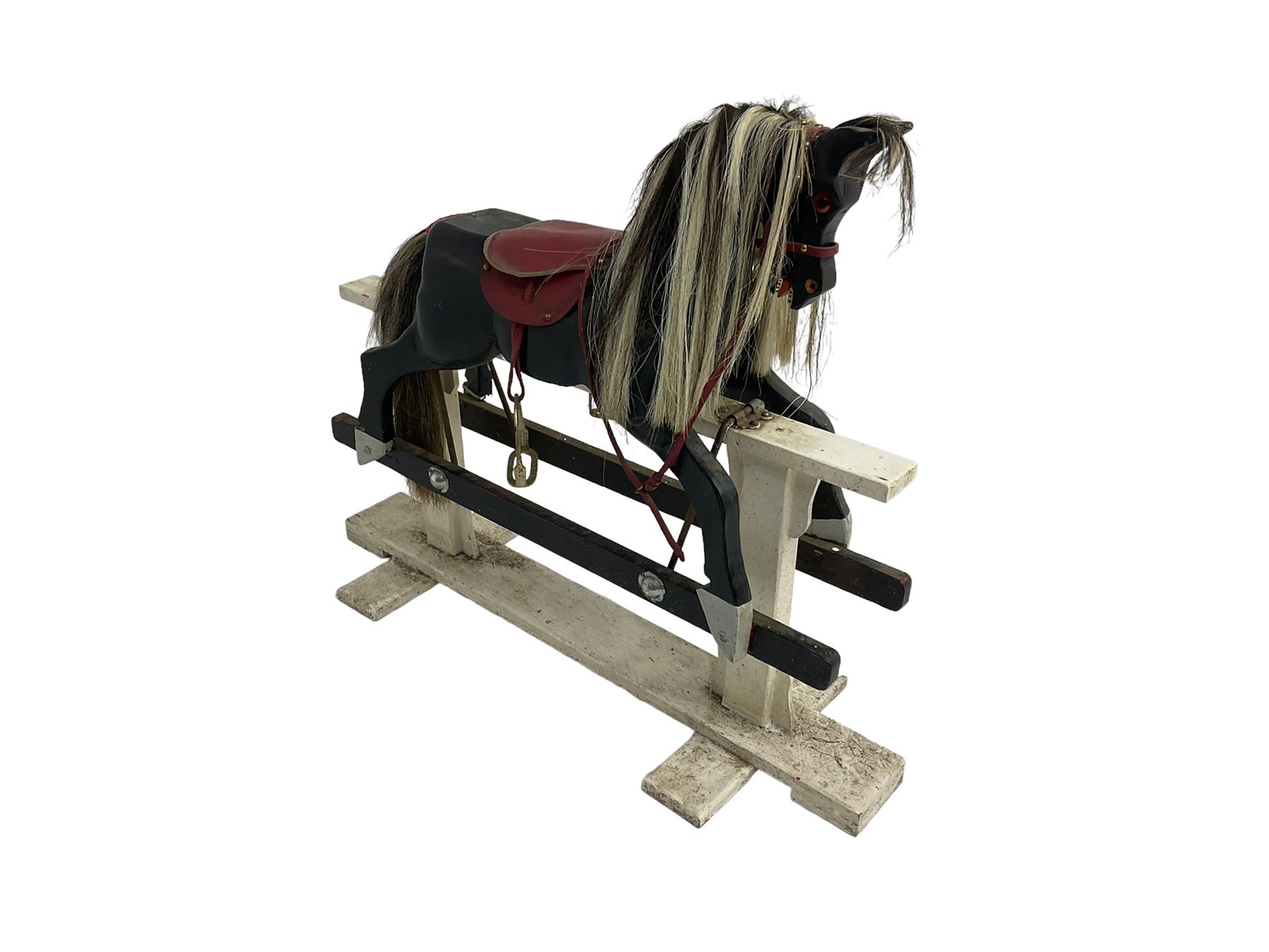 20th century black painted rocking horse on white painted trestle base, fitted with saddle and stirrups 