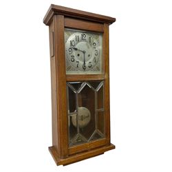 German - Art Deco oak cased 8-day wall clock c 1930, with a moulded flat top and fully glazed door, deeply cut bevelled glass panels and visible pendulum, silvered dial with Art Deco design spandrels, Arabic numerals, minute track and spade hands, twin train movement striking the hours and half hours on four gong rods. With pendulum and key.  