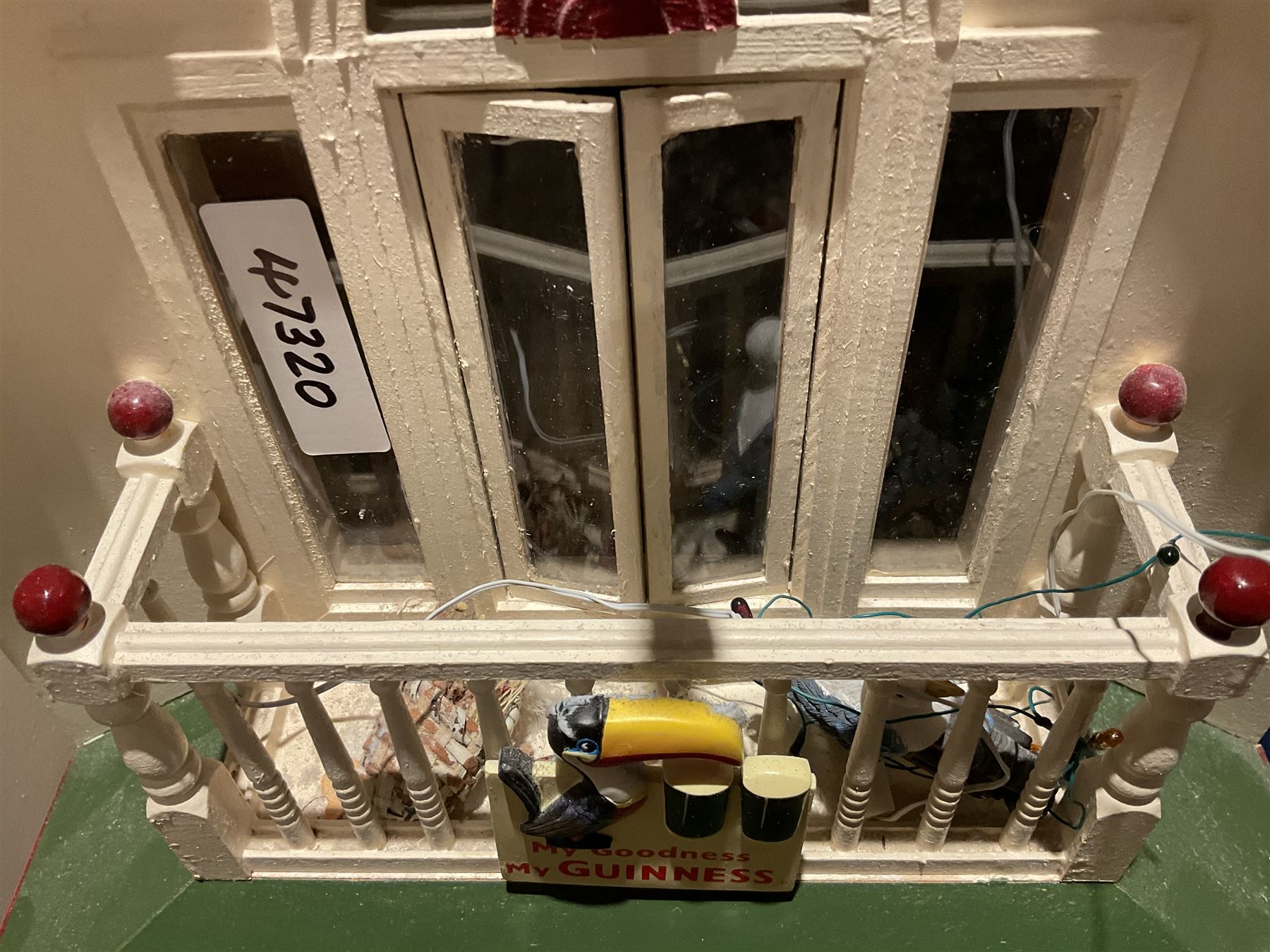 Seagull Pub - scratch-built wooden doll's house as a two-storey gable fronted public house painted in white green and maroon; the hinged front with ground floor veranda and window over opening to reveal two fully furnished rooms with dog-leg staircase and well stocked bar with bar-tender L31cm H62cm D37cm; together with Corner Shop and Dollies Pantry; a similarly painted scratch-built wooden two-storey flat-roofed doll's house as a well stocked ground floor grocery shop with stairs up to two further fully furnished rooms and more stairs giving access to a roof terrace L46cm H57cm D33cm (2)