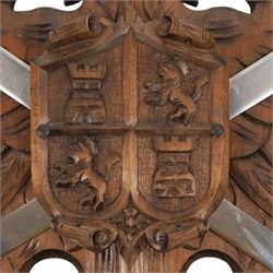 Carved wooden wall plaque, decorated with foliate scrolls, with two reproduction swords attached, together with five other wooden plaques with foliate scrolls and shields