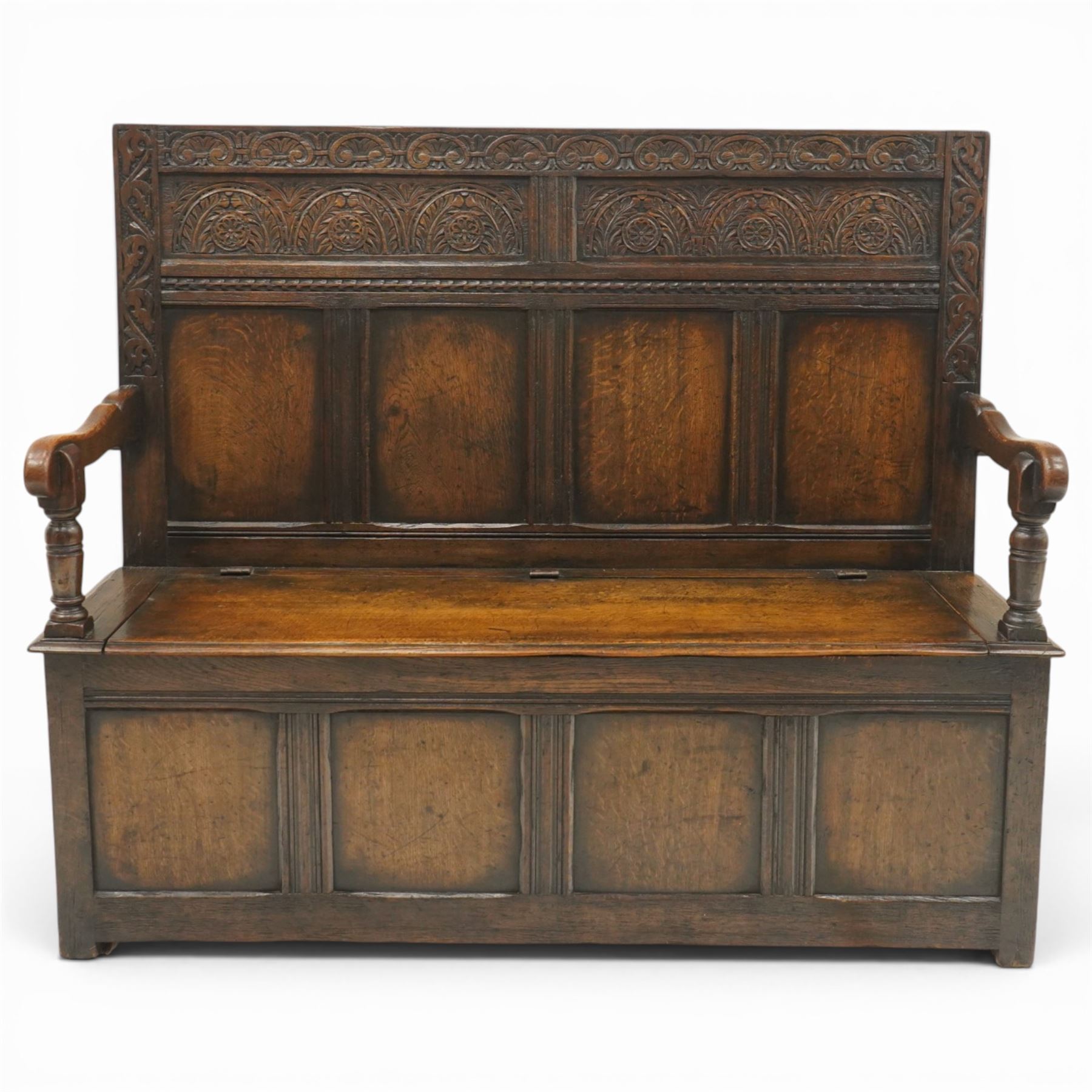 Victorian Jacobean Revival carved oak settle or hall bench with box seat, the cresting rail carved with repeating lunette motifs with acanthus and rosette decoration, over four back panels and hinged box seat, the panelled base raised on stile supports