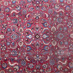 Persian Mashad design wool carpet, the red ground with dense scrolling floral and foliate decoration, within dark blue main border decorated with repeating palmettes and shaped leaves