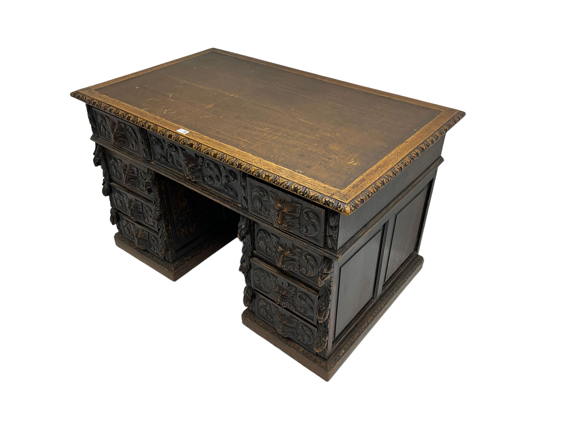 Late 19th century Gothic revival carved oak twin pedestal desk, rectangular top with inset writing surface and carved edges, central frieze drawer flanked by eight drawers, all with green man carved handles and extending trailing foliage, carvings of pineapple and lion mask corbels, the pedestals with panelled sides and back, on plinth bases