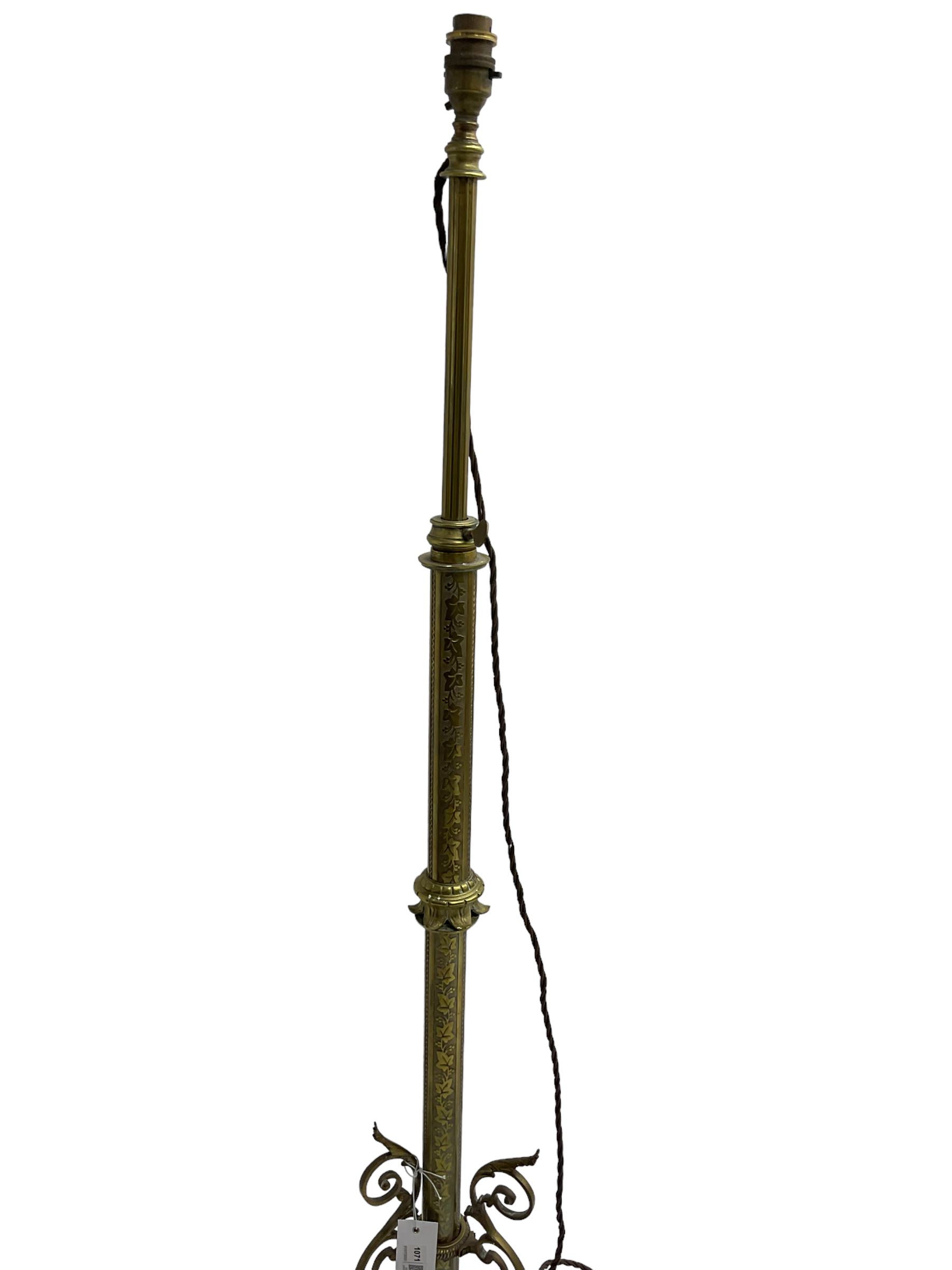 Victorian brass floor standing oil lamp, column decorated with ivy and acanthus leaves, the tripod base pierced with scrolled foliate decoration, with ivory and gilt shade, later converted to electricity