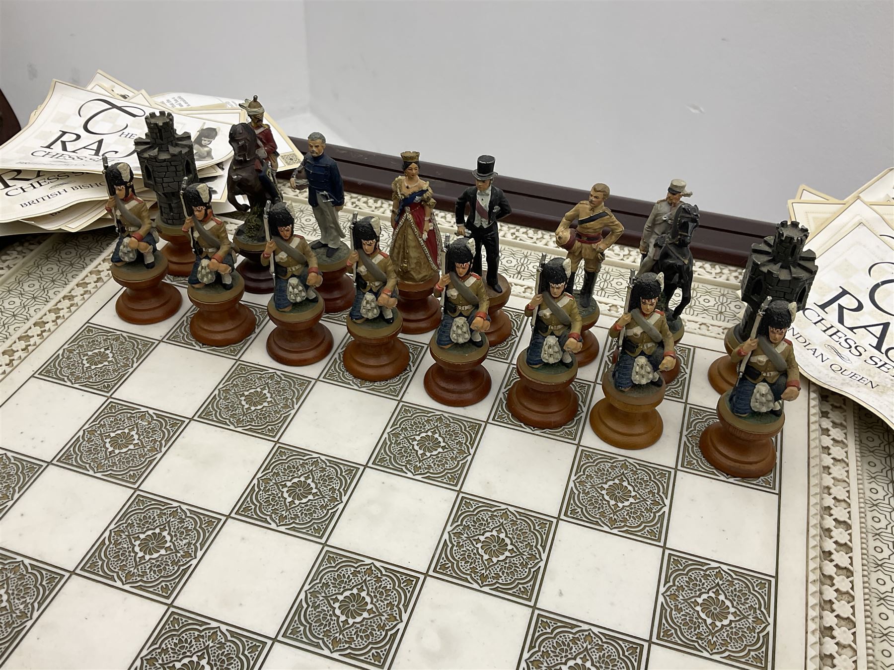 Franklin Mint Indian ' The Raj ' chess set with marble effect chess board within a mahogany stained frame raised on a brass mounted pedestal base with single fitted drawer, the playing pieces depicting figures from the 1857 Raj mutiny 52cm square H68cm