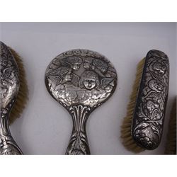 Edwardian silver mounted dressing table items, comprising hair brush, hand mirror and two clothes brushes, each repousse embossed with cherub groups, hallmarked with various dates and makers