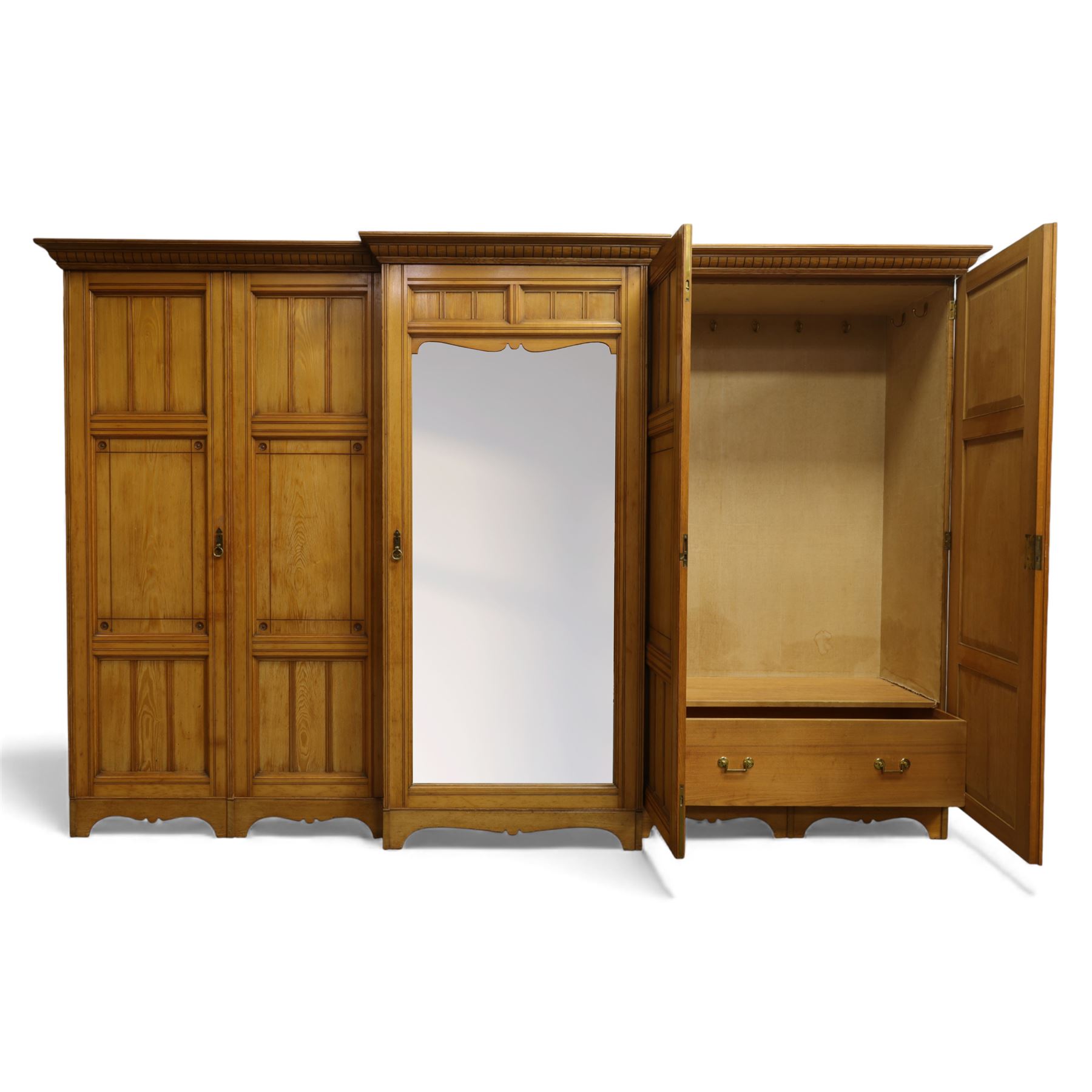 Gothic revival ash breakfront wardrobe in the manner of Charles Bevan, the four fielded panelled doors flanking a central mirrored door, opening to reveal an fitted interior with hanging rails and compartment shelves and drawers, upon a shaped plinth base with bracket cut feet

