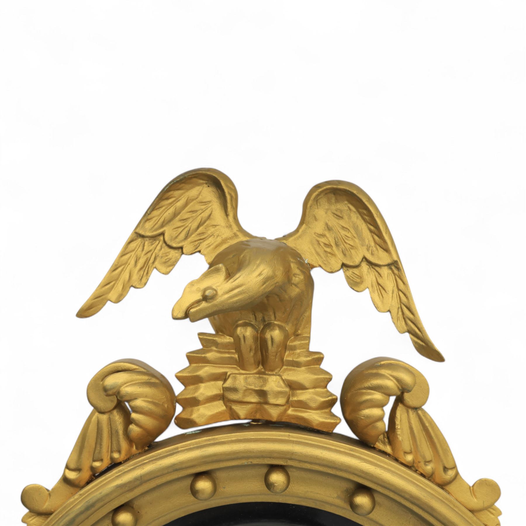 Early 20th-century Regency-style giltwood convex mirror, circular plate within a ball-mounted frame surmounted by an eagle cresting and flanked with scrolls, apron carved with foliate decoration 