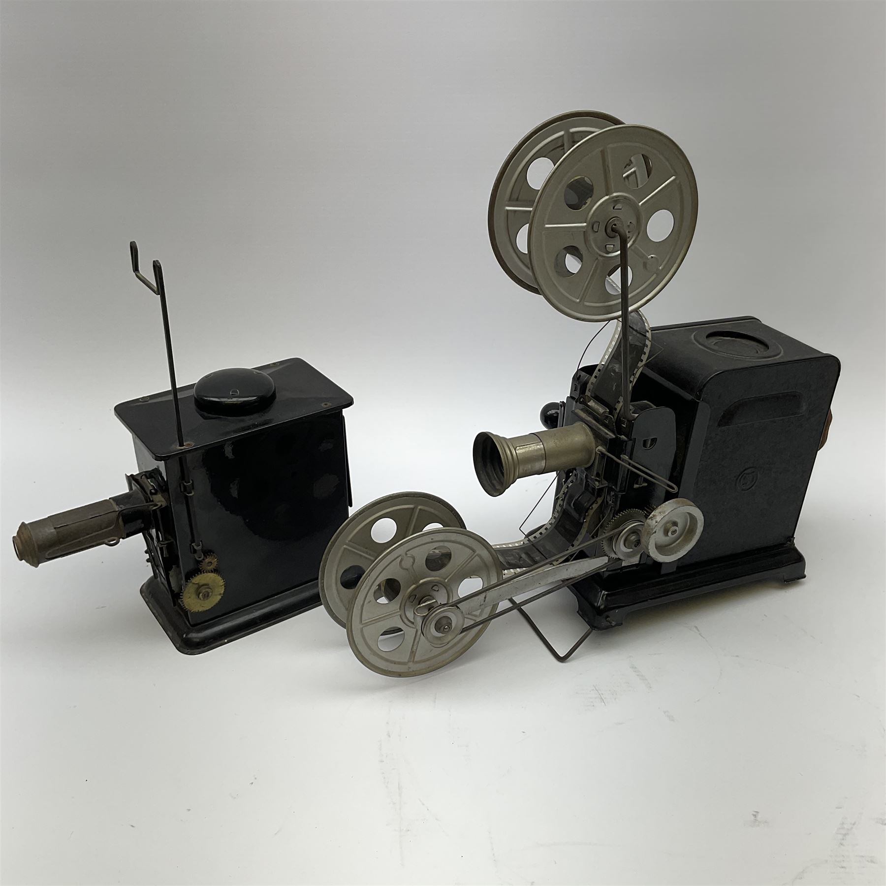 Early 20th century tinplate combined magic lantern and 35mm cinematograph projector, hand-cranked, with electric bayonet lamp, fitted with film reels, L35cm overall, and a similar projector by Gebruder Bing Nuremberg with spirit lamp (glass chimney a/f) L22cm, with two reels of film 