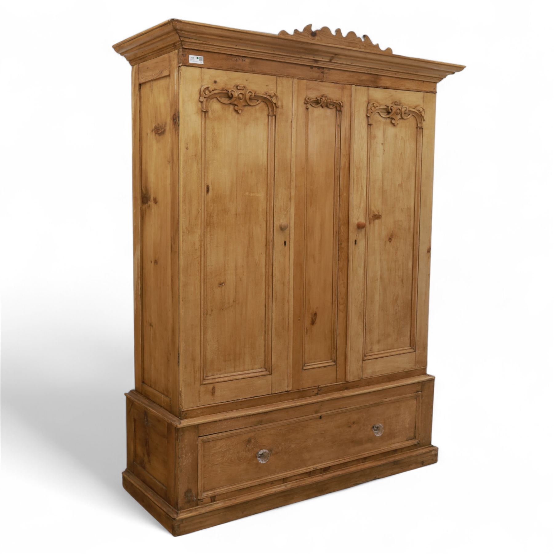 Late 19th century pine wardrobe, with stepped cornice over triple panelled doors, applied foliate carvings to outer panels, raised over a separate pine plinth drawer with moulded facia and twin glass pulls
