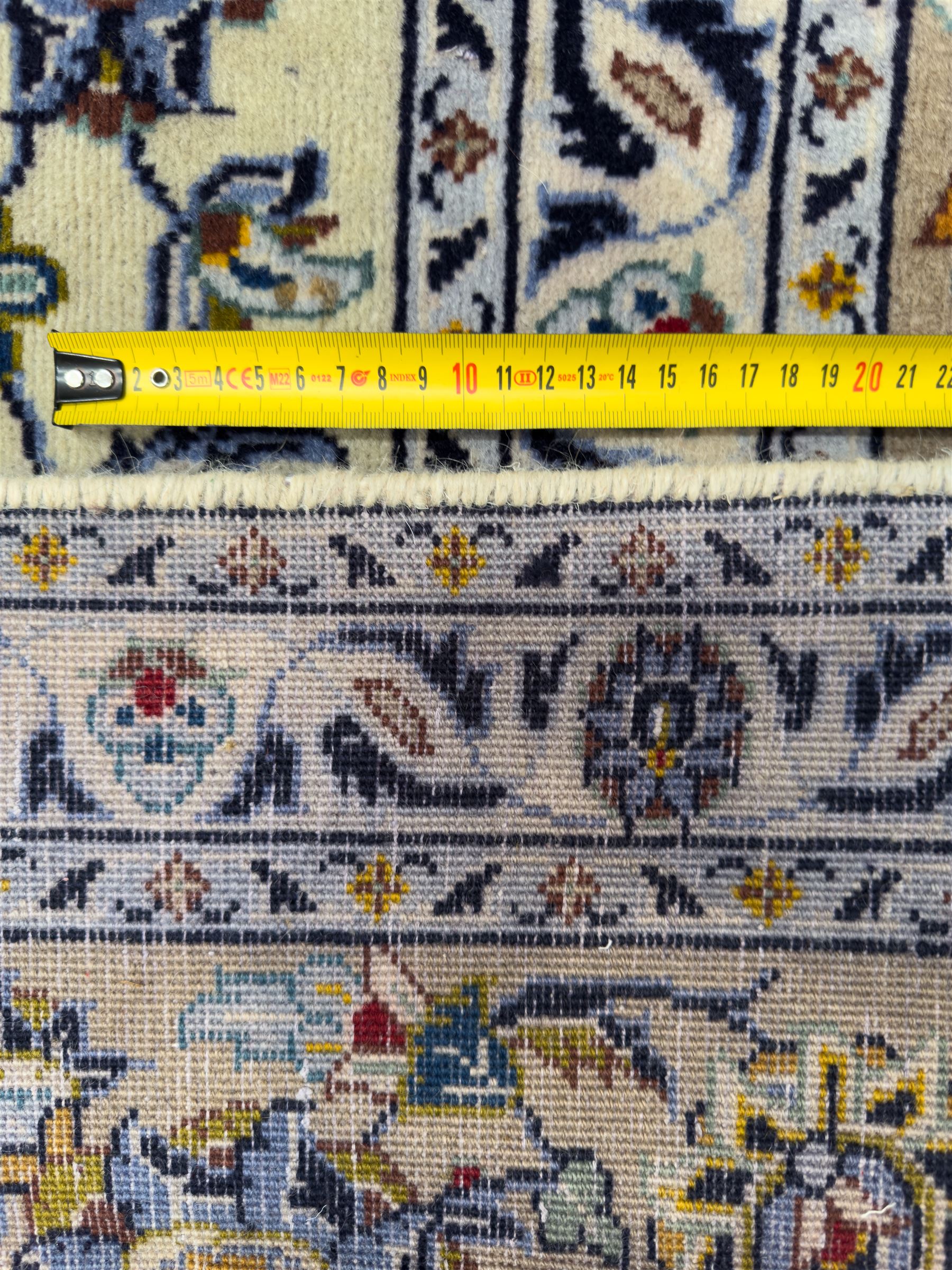 Central Persian Kashan hand-knotted carpet, ivory field with an all-over design of scrolling vines, lotus palmettes, and rosettes in shades of blue, gold, and brown within a blue ground border of palmettes and arabesques between multiple guard stripes