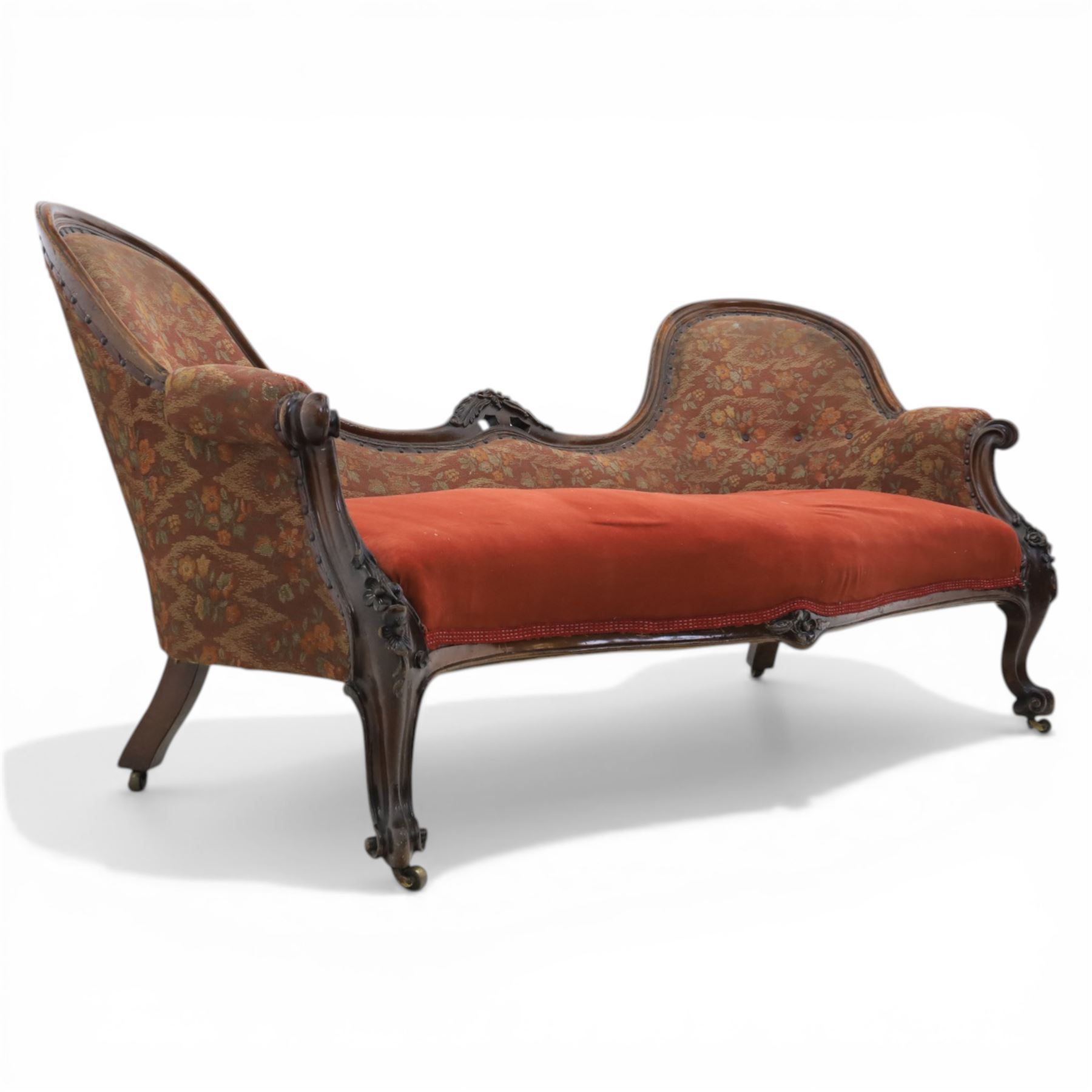 Victorian mahogany framed serpentine sofa, the shaped button upholstered back with central carved foliate cartouche, and scroll arms with carved terminals, over upholstered red seat, upon carved cabriole supports with castors