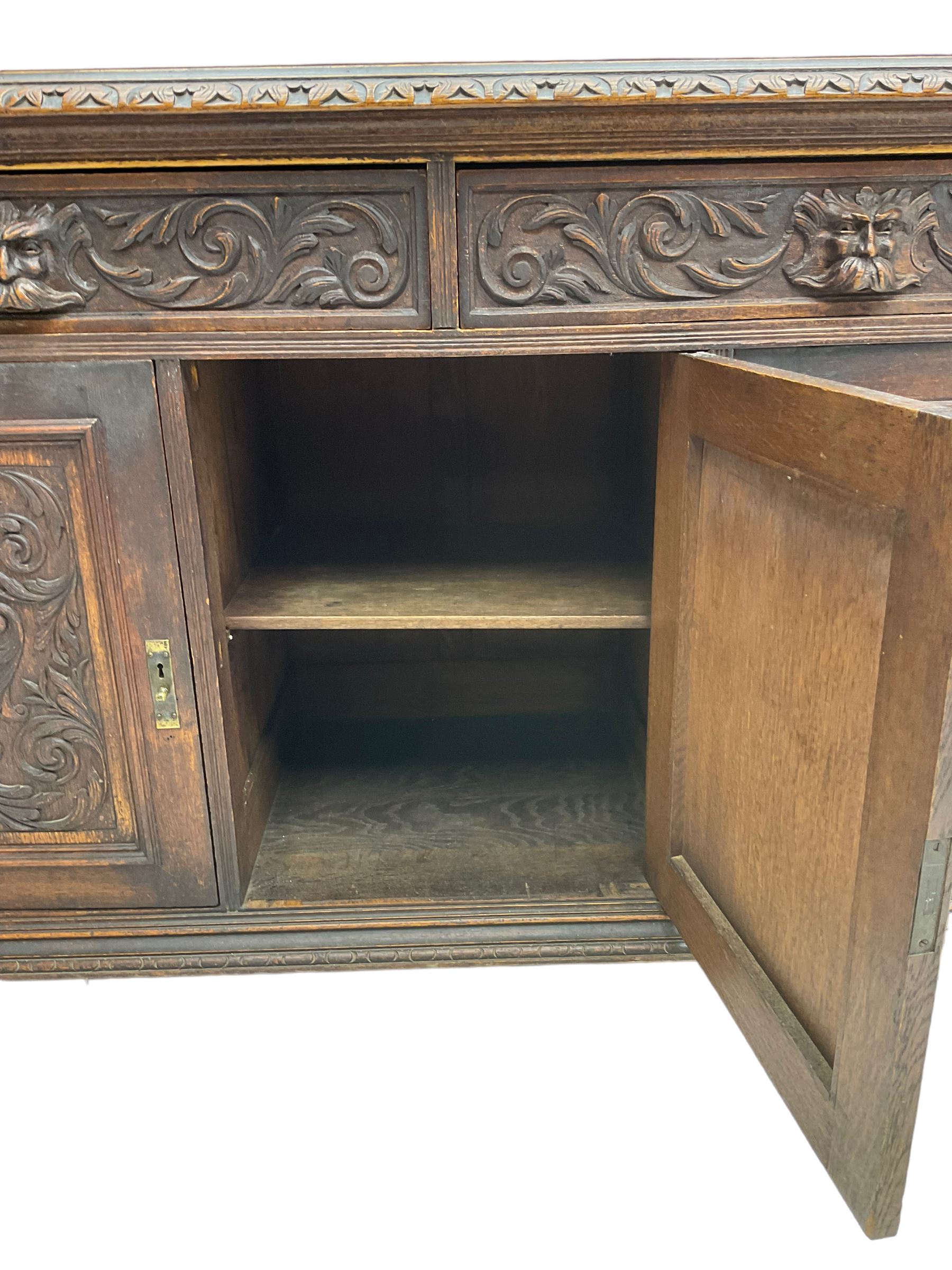 Victorian heavily carved oak sideboard, the moulded top carved with foliate decoration to the edge, fitted with two drawers and three cupboards, the drawer fronts carved with green man mask handles and scrolling foliage, the panelled doors carved with interlacing foliage, on turned compressed bun feet