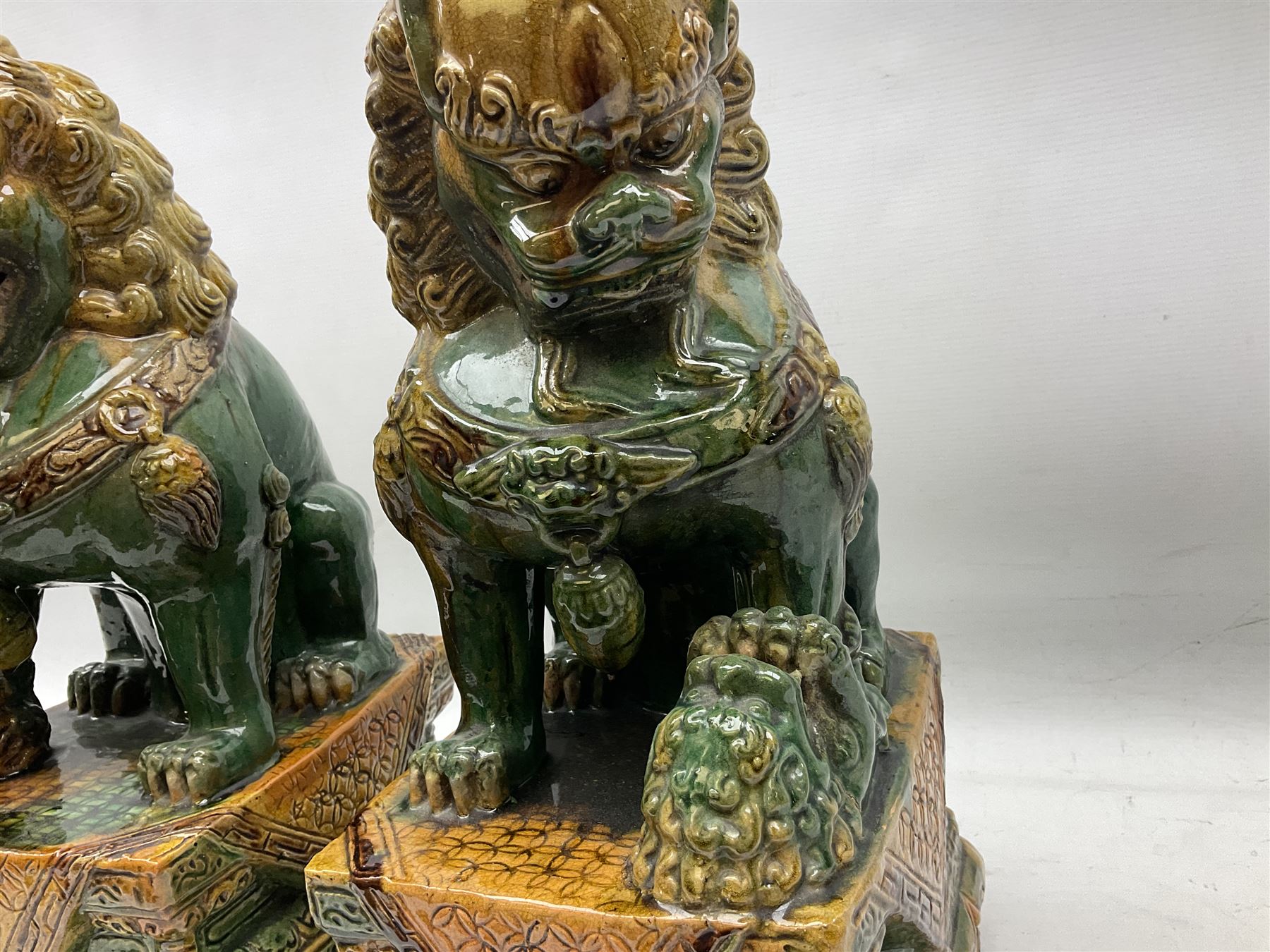 Pair of Chinese Temple Lions or Dogs of Foo, modelled in seated post, one with one front paw resting upon a ball, the other upon a cub, each upon stylised plinth base, H44cm