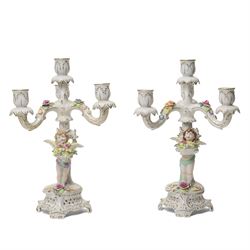 Pair of German porcelain three branch candelabra, the based modelled with putti holding fl...