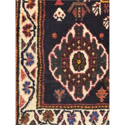 Persian Qashqai crimson ground runner, the field decorated with repeating diamond-shaped medallions flanked by angular floral motifs, the spandrels with intricate boteh designs, framed by an ivory border with stylised floral patterns and scrolling vines