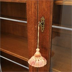 Late 20th century oak bookcase on cupboard, with moulded cornice above pair of astragal glazed doors with shaped inner frames enclosing adjustable shelves, the base with moulded top above two fielded panel cupboard doors with brass handles, upon compressed bun front feet 