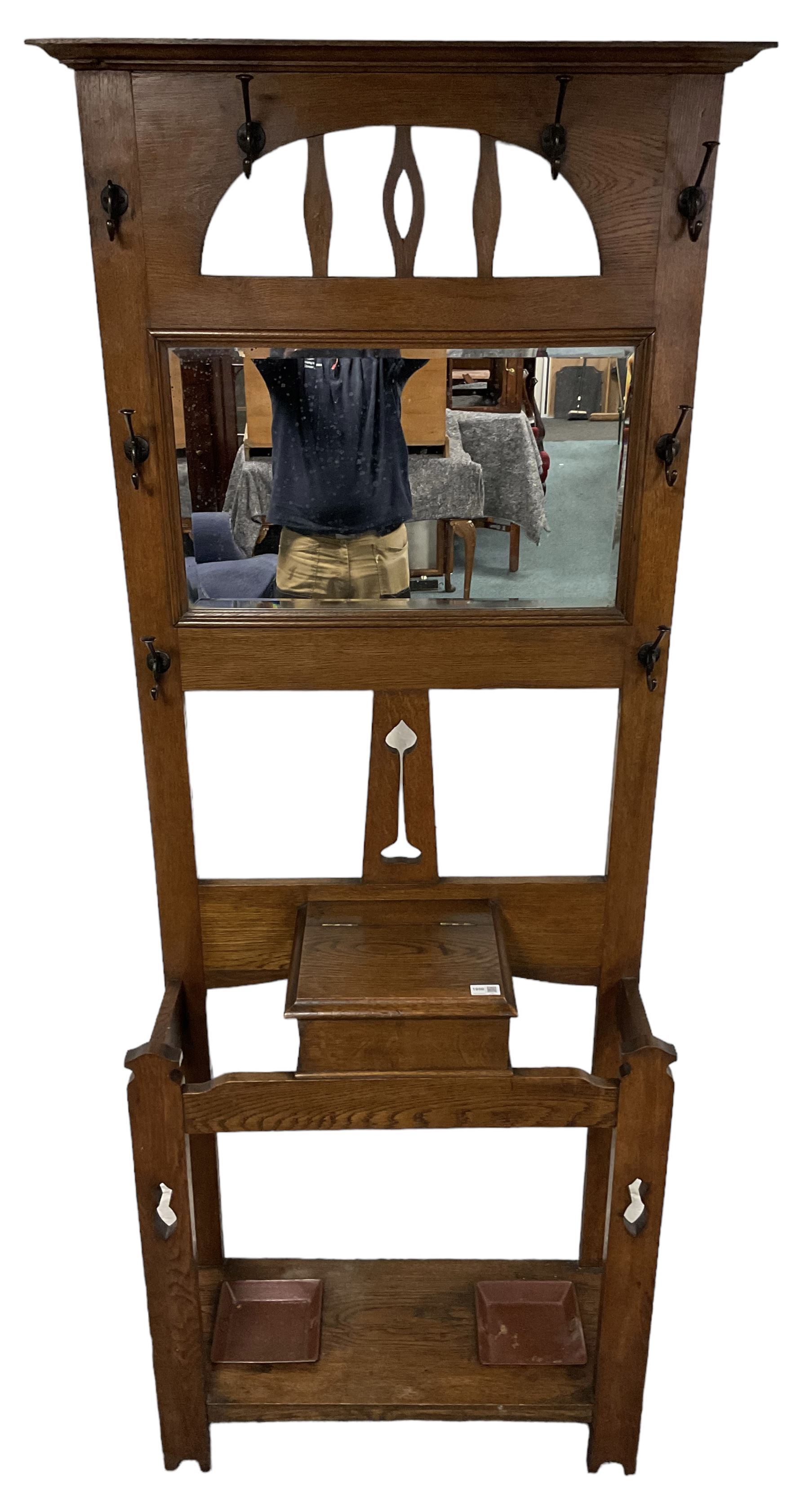Arts & Crafts period oak hall stand, projecting moulded cornice over arched cut-out decorated with shaped vertical rails, fitted with rectangular bevelled mirror back over hinged glove compartment, on straight pierced supports with shaped pediments 
