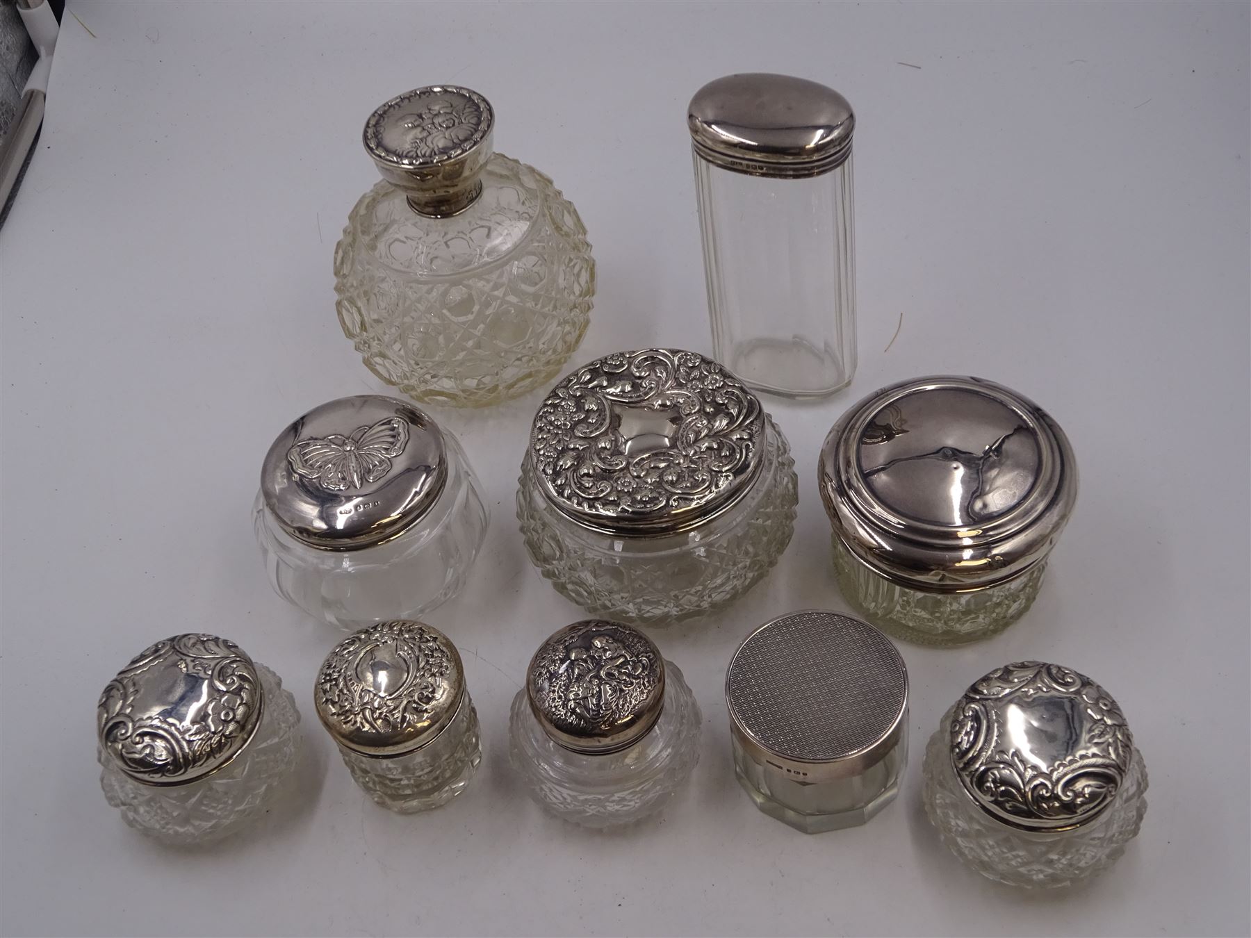 Mid 20th century silver topped cut glass scent bottle, with hobnail and octagonal decoration to the glass body, the silver lid repousse decorated with putti, hallmarked Boots Pure Drug Company, Birmingham 1943, together with nine silver topped glass dressing table jars, with designs including butterfly and romantic scene,  all with hallmarked with various makers and dates