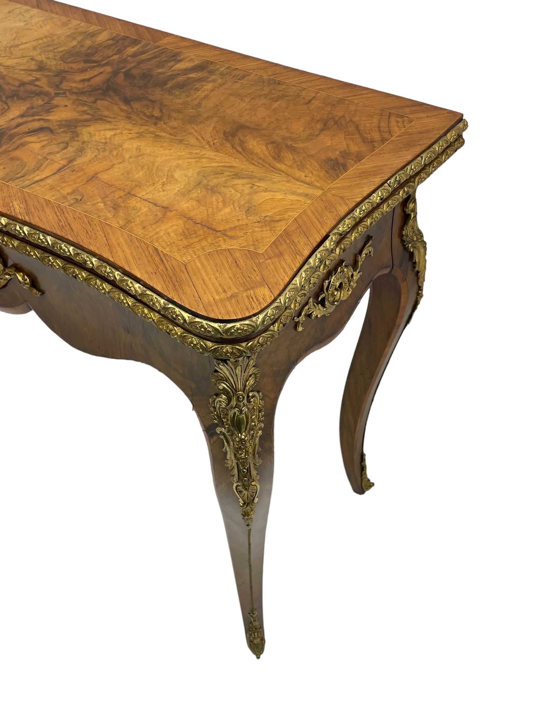 20th century French walnut and Kingwood card table, shaped fold-over top with figured quarter-matched veneers and floral egg and dart moulded edge in gilt metal, shaped aprons decorated with shell motifs with extending foliage, pull-out action base revealing storage well, on cabriole supports with ornate gilt metal mounts 