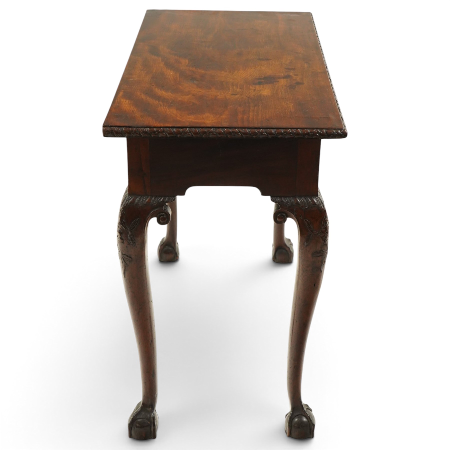George I carved mahogany side table, adapted from a card table, the rectangular top with foliate-carved edge above a plain frieze, raised on cabriole legs with acanthus-carved knees, volute brackets and floral-carved motifs, terminating to ball-and-claw feet