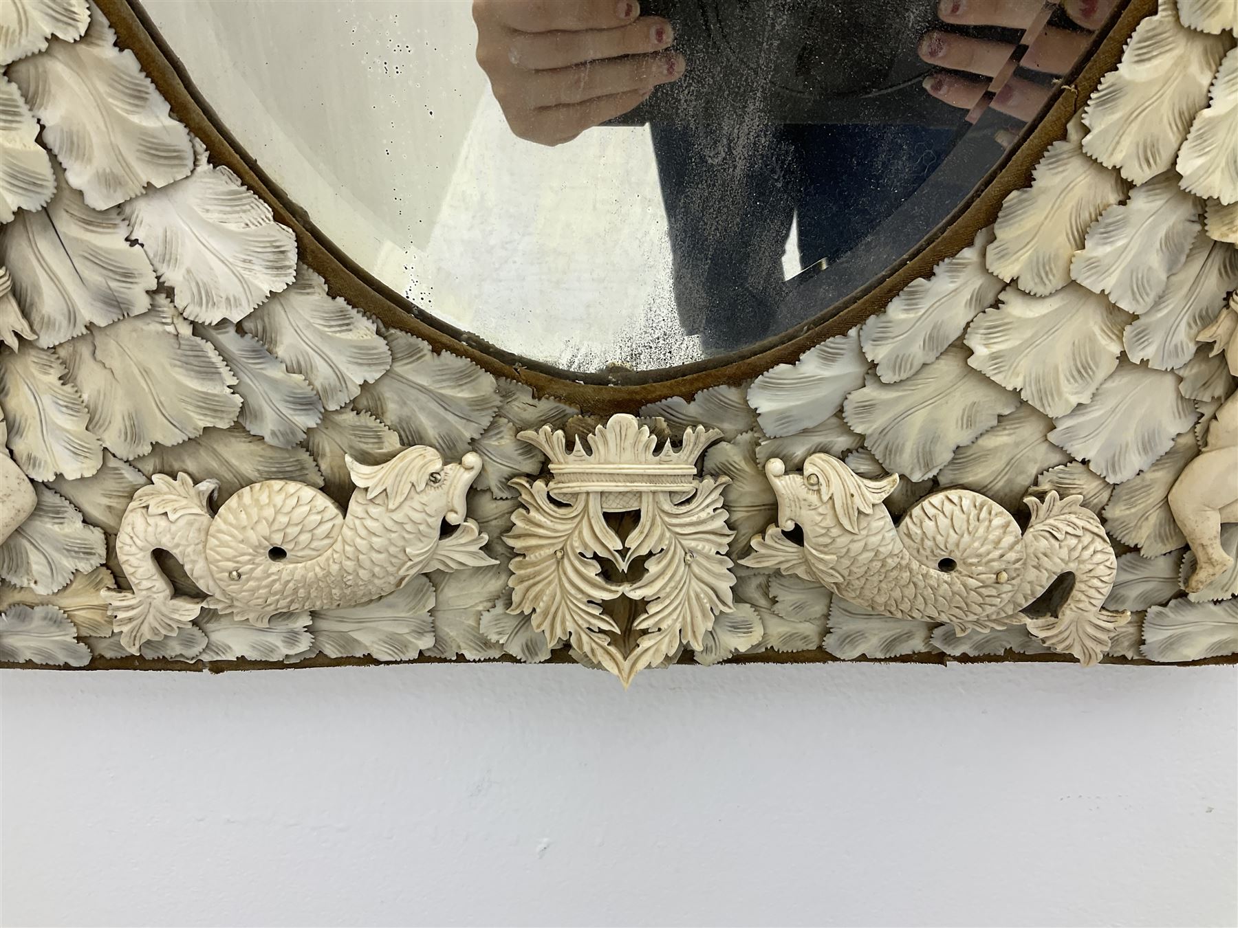 Pair 19th century French Dieppe bone and ivory wall mirrors, the oval bevelled mirror plates within rectangular frames with shaped tops, profusely decorated with ivory leaves, further detailed with carved bone armorial type crest inscribed 'SGOTORVM', putti, fish and mask heads, H81cm W48cm
