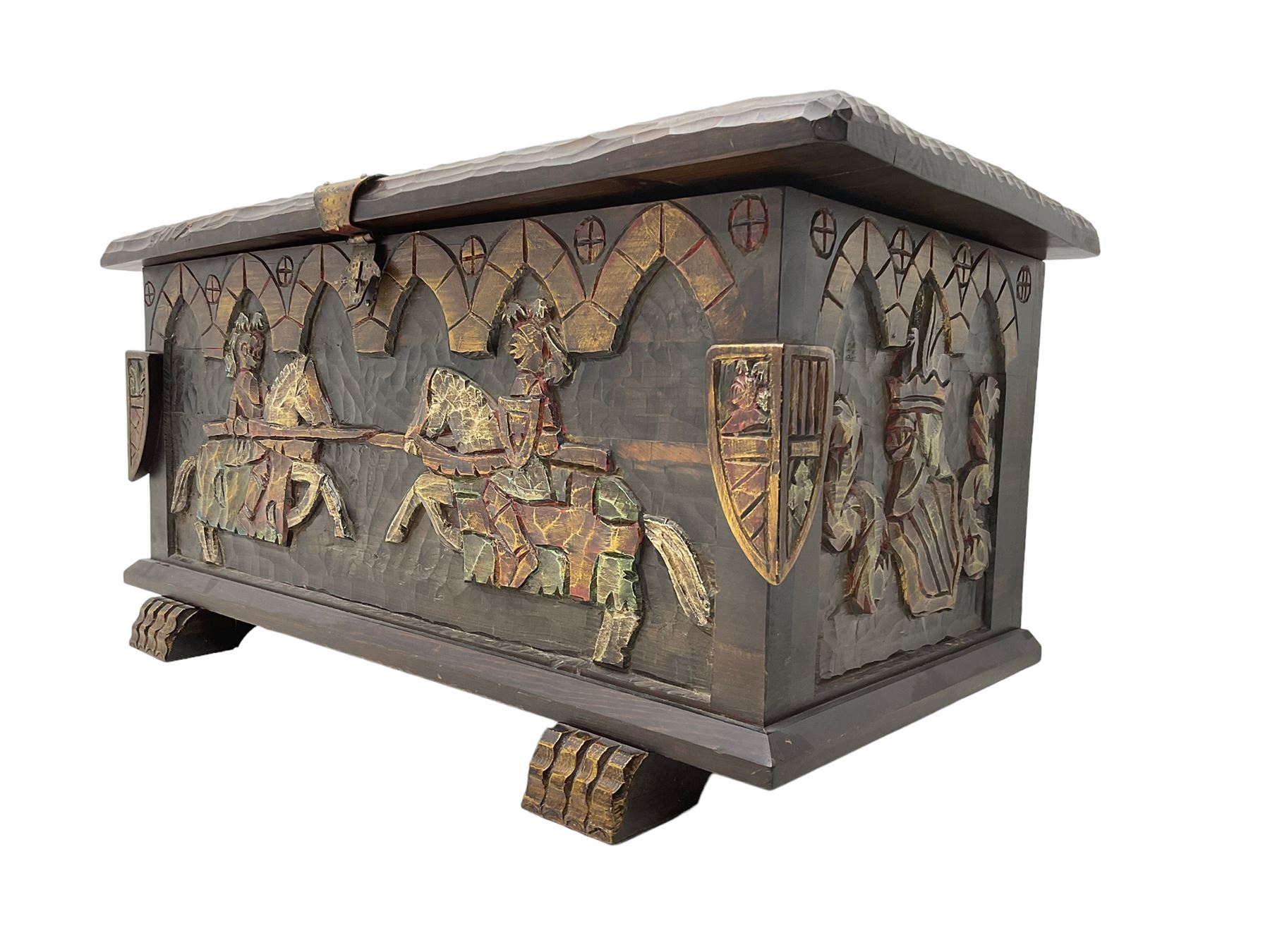 Carved wooden blanket chest, the tooled hinged lid with shaped metal strap hinges and catch, the front carved with arcade over two medieval jousters, on carved sledge feet