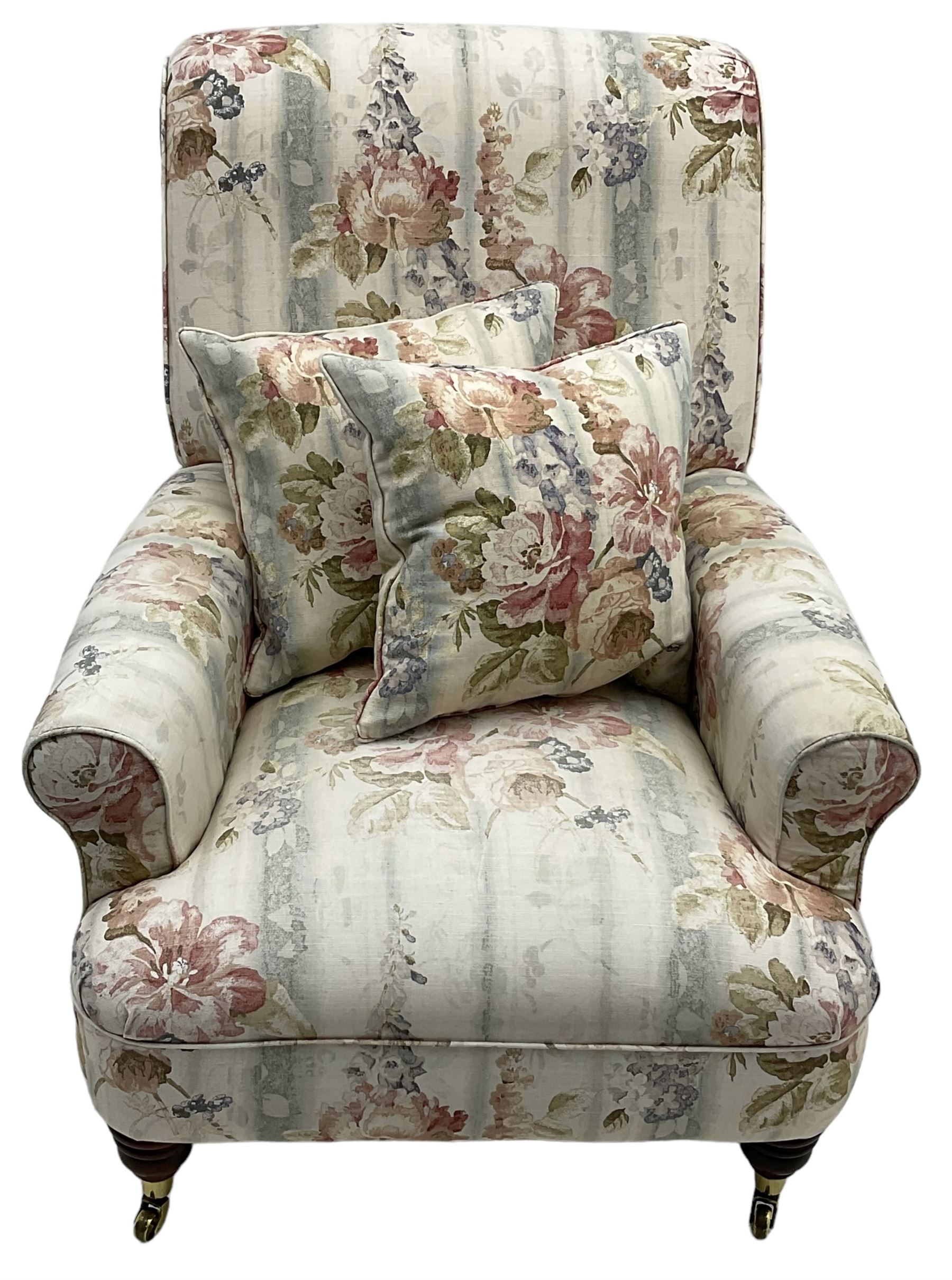 Victorian design armchair, rolled back and arms, upholstered in floral pattern fabric with two scatter cushions, on turned front feet with brass cups and castors