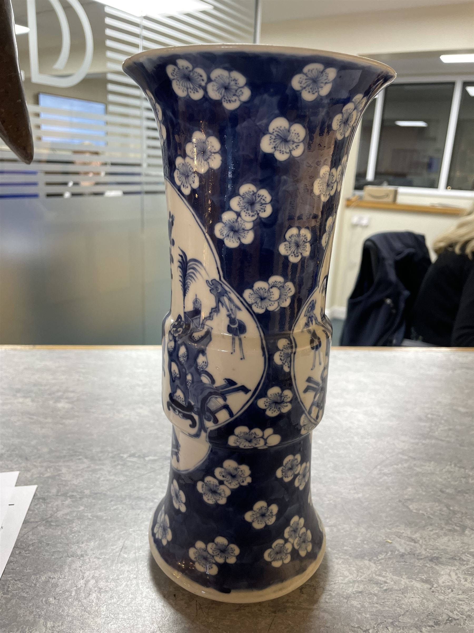 Late 19th century Chinese blue and white gu beaker vase, decorated with two lobed reserves containing precious objects, against a prunus and cracked ice ground, with apocryphal Kangxi mark beneath, H30.5cm