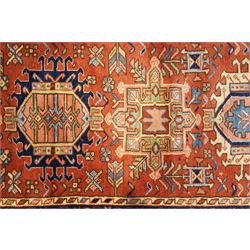 North West Persian Karajeh hand-knotted runner, field decorted with a series of linked stepped hexagonal medallions encloing stylized geometric motifs, surround by angular floral and tribal devices on a terracotta red ground enclosed a navy main border of repeating geometric and rosette motifs, between multiple guard stripes, with cotton fringe ends 