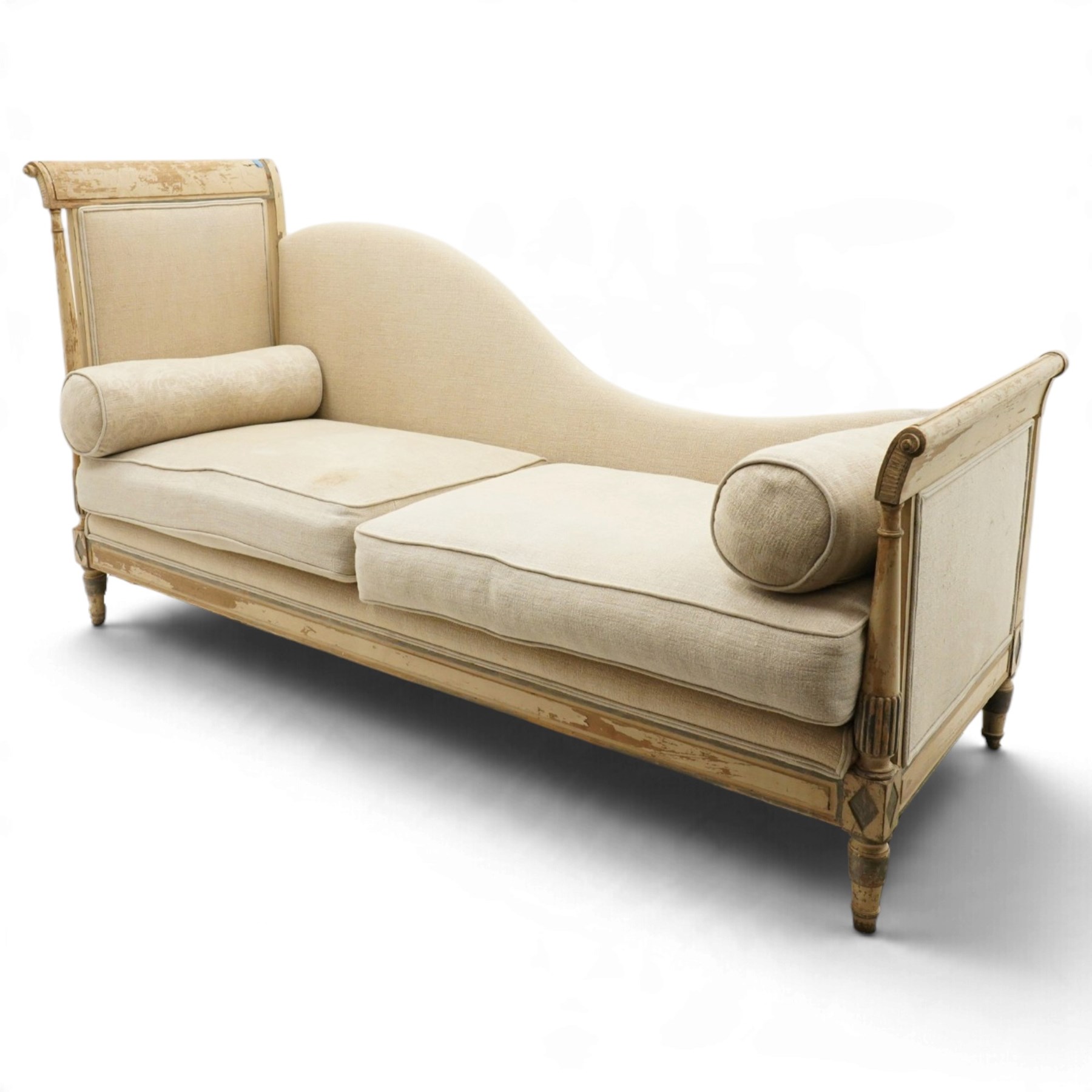 19th century French painted day bed, asymmetrical scrolled ends flanking a serpentine upholstered back, with upholstered end panels, loose seat cushions and cylindrical bolsters upholstered in beige fabric, with turned uprights with fluted detailing, moulded seat rail and lozenge-moulded corner blocks, raised on turned tapering supports