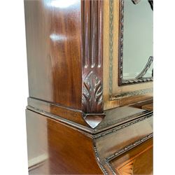 Large and impressive late 19th century Irish mahogany secretaire bookcase, moulded sloped arch dentil pediment decorated with central carved mask surrounded by linen festoons and trailing bellflowers, canted and fluted uprights with carved acanthus leaf upper and lower brackets, enclosed by two astragal glazed doors in the form of trophies with twist ribbon carved mouldings, inlaid with fanned spandrels and trailing leaf painted satinwood band, cylinder roll top inlaid with central fan motif and fanned spandrels, pull-out action revealing stepped fitted interior, central tambour roll cupboard flanked by two Composite pilasters and a combination of drawers and pigeon holes, fitted with three break-front drawers, matched canted and fluted corners with acanthus leaf carvings, on square tapering and fluted spade feet