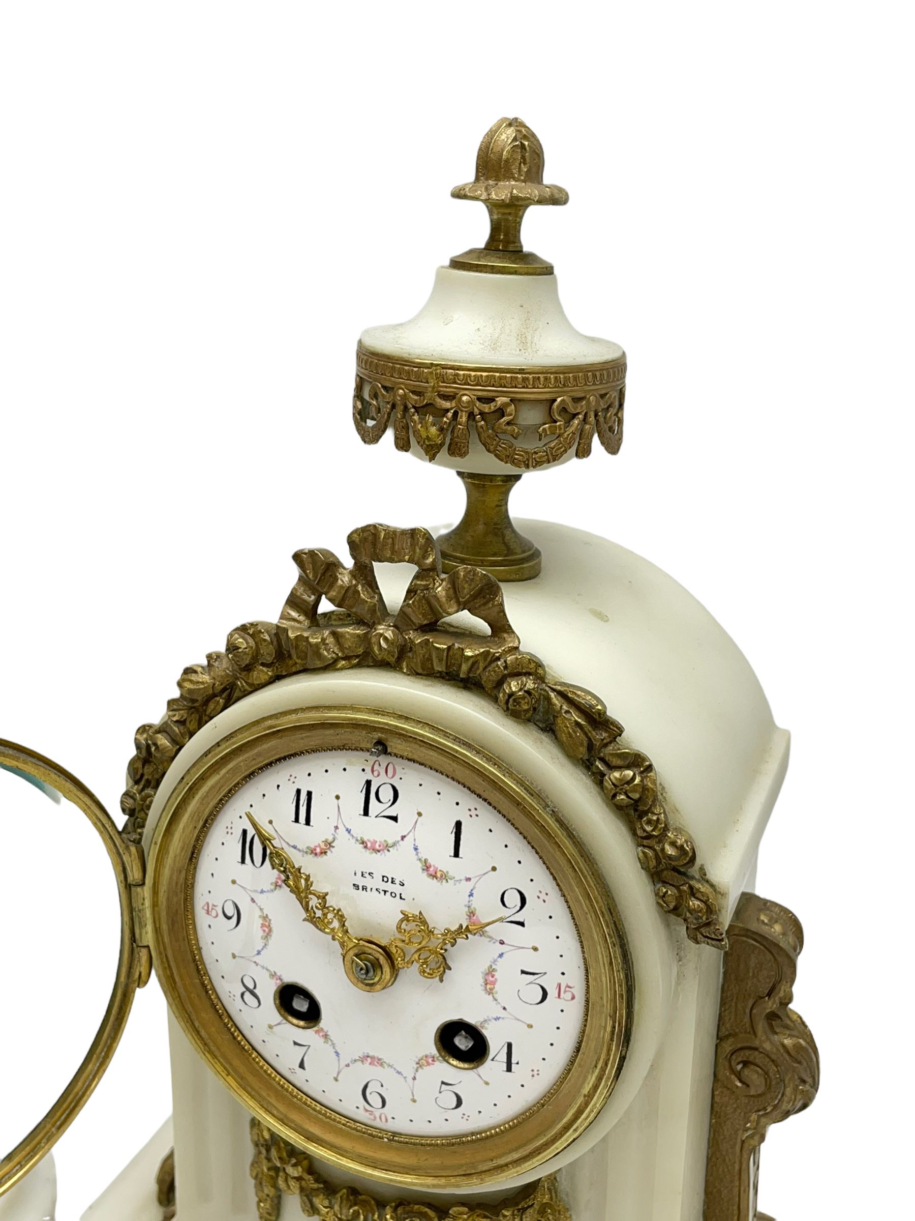 An early 20th century white marble mantle clock in a break front case with an arched top and finial, gilded scroll work to the sides and pierced foliate panels to the front, plinth raised on five bun feet, enamel dial with garland decoration, Arabic numerals, minute markers and Louis XV gilt hands, within a convex glazed bezel, eight-day Parisian striking movement striking the hours and half hours on a bell, with two conforming single light candlesticks. With Pendulum.

