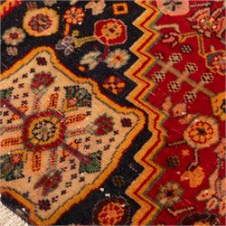 North Persian crimson ground rug, the field densely decorated with stylised flowering plants, urns and polychrome rosettes, within a stepped ochre outline, dark ground floral spandrels and geometric side panels