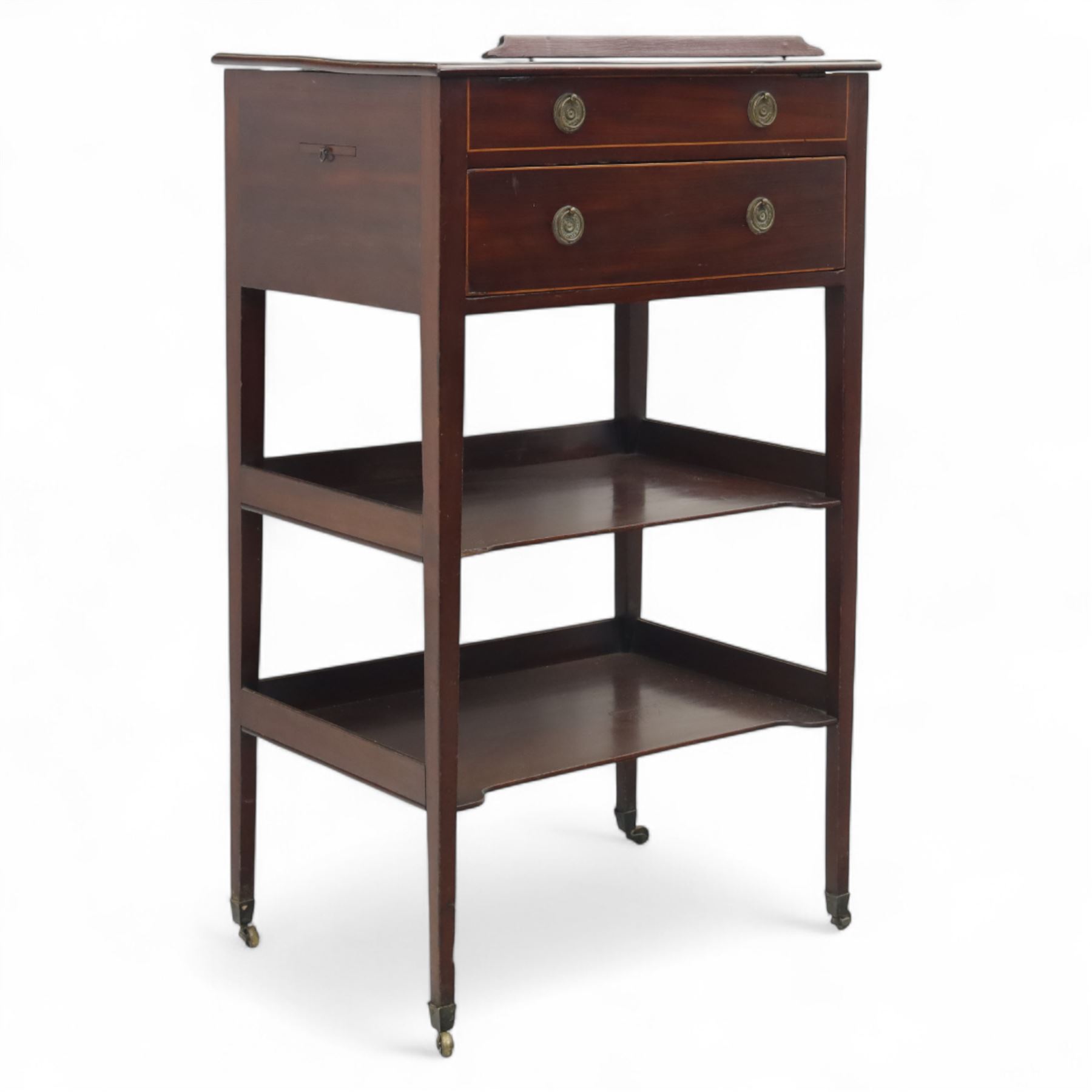 George III mahogany and boxwood-strung drawing table, the rectangular sloping reading surface with rest and oak stay, above a blind drawer and a drawer fitted with brass ring handles, side with pull-out candleholder and inkwell compartment, raised on square-section tapered legs with brass box castors united by two galleried under tiers