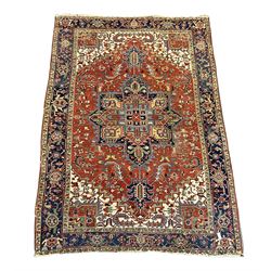 Persian Heriz carpet, the red ground field decorated with geometric star medallion surrounded by interlaced foliate and stylised plant motifs, repeating guarded border decorated with flower heads