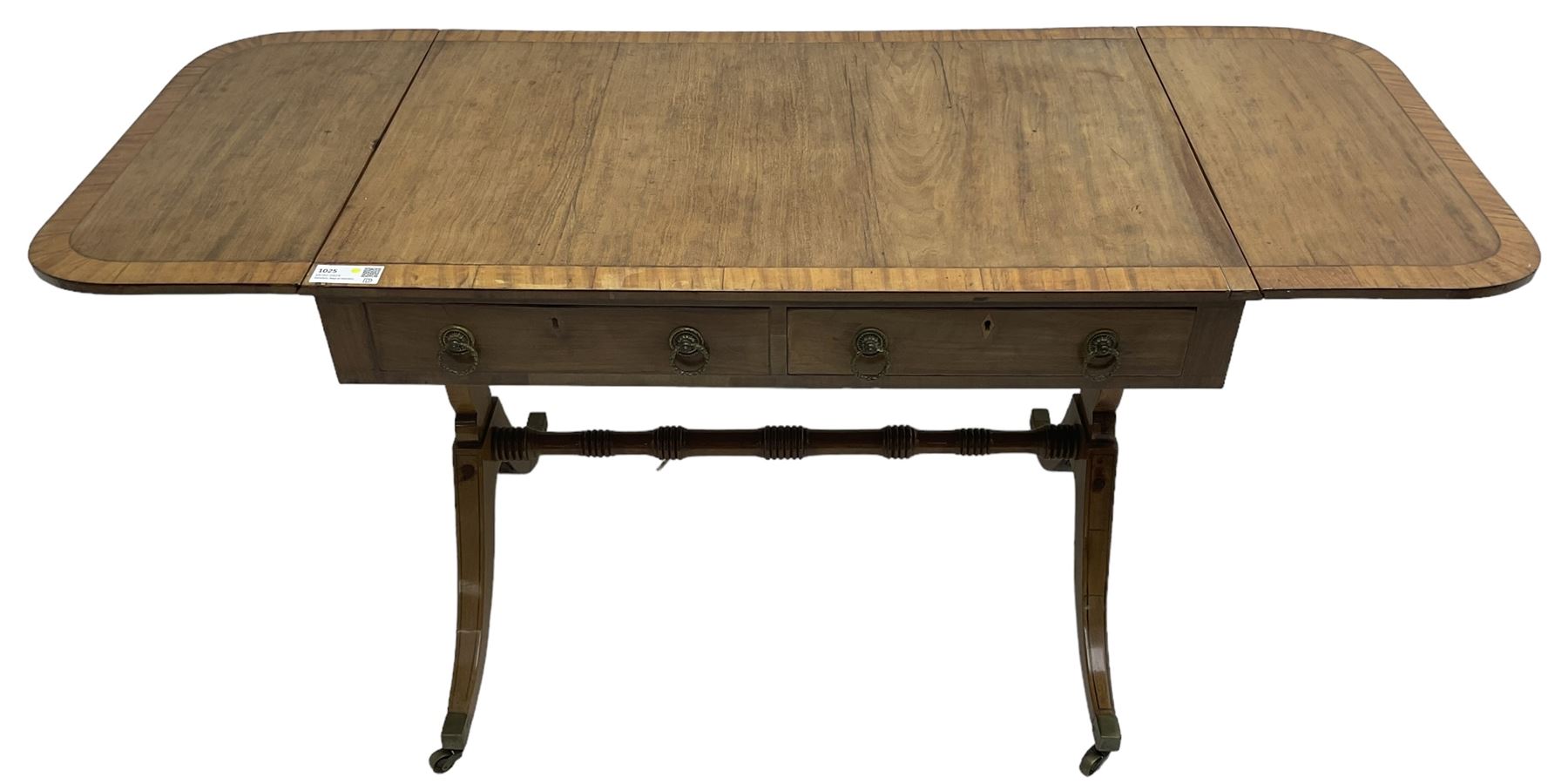 Regency mahogany sofa table, rectangular crossbanded top with twin drop-leaf ends, fitted with single drawer and one faux drawer, raised on shaped end supports united by ring turned stretcher