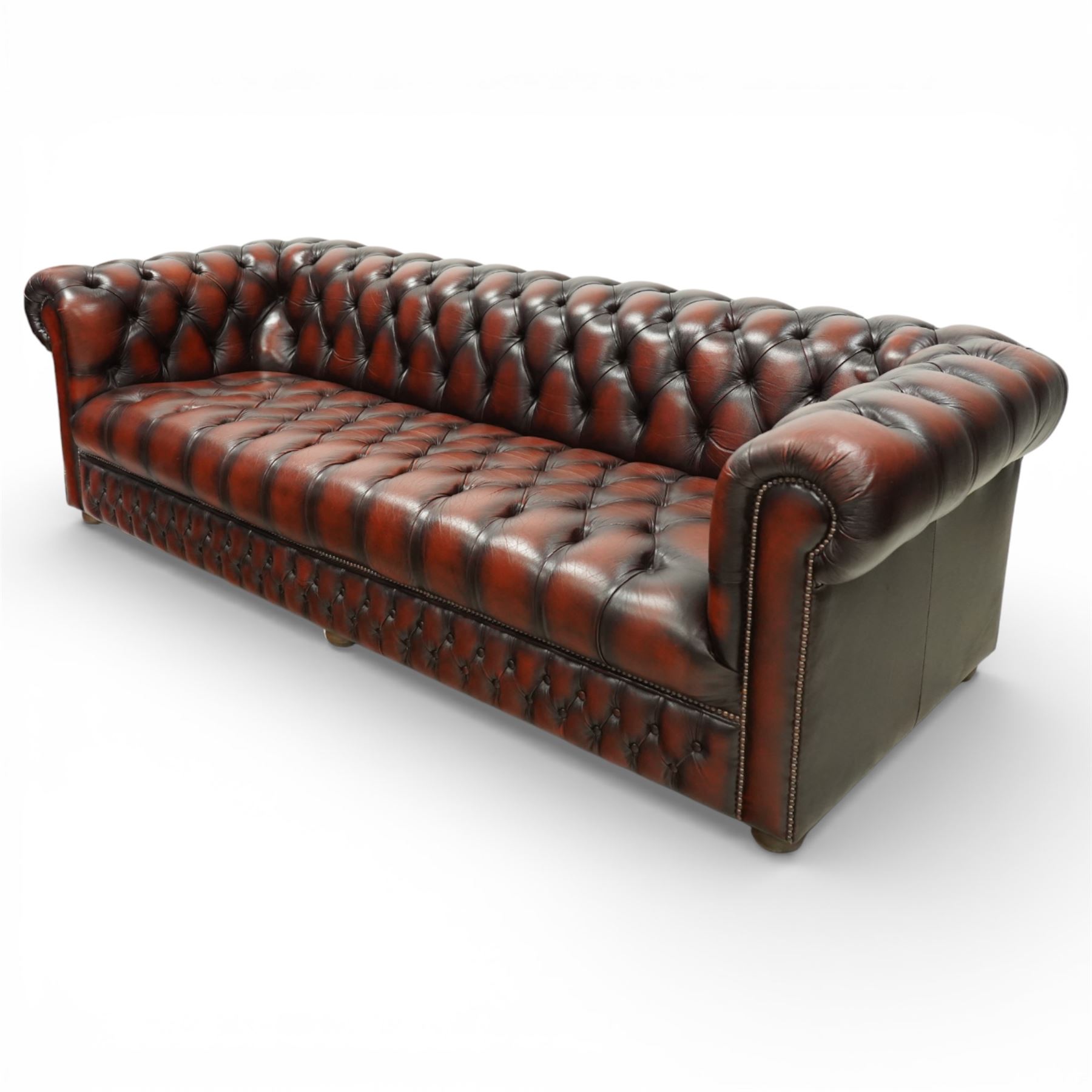 Late 20th century four seat Chesterfield sofa, upholstered in deep buttoned brown leather, with rolled arms, buttoned back and seat, studded detailing and squat feet