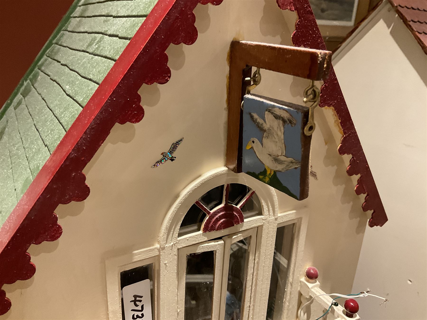 Seagull Pub - scratch-built wooden doll's house as a two-storey gable fronted public house painted in white green and maroon; the hinged front with ground floor veranda and window over opening to reveal two fully furnished rooms with dog-leg staircase and well stocked bar with bar-tender L31cm H62cm D37cm; together with Corner Shop and Dollies Pantry; a similarly painted scratch-built wooden two-storey flat-roofed doll's house as a well stocked ground floor grocery shop with stairs up to two further fully furnished rooms and more stairs giving access to a roof terrace L46cm H57cm D33cm (2)